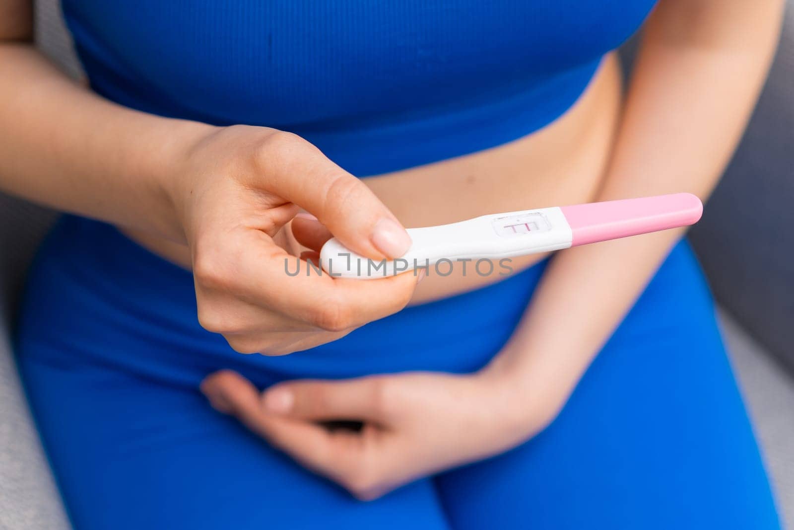 Woman in blue holding a positive pregnancy test and holding the belly.