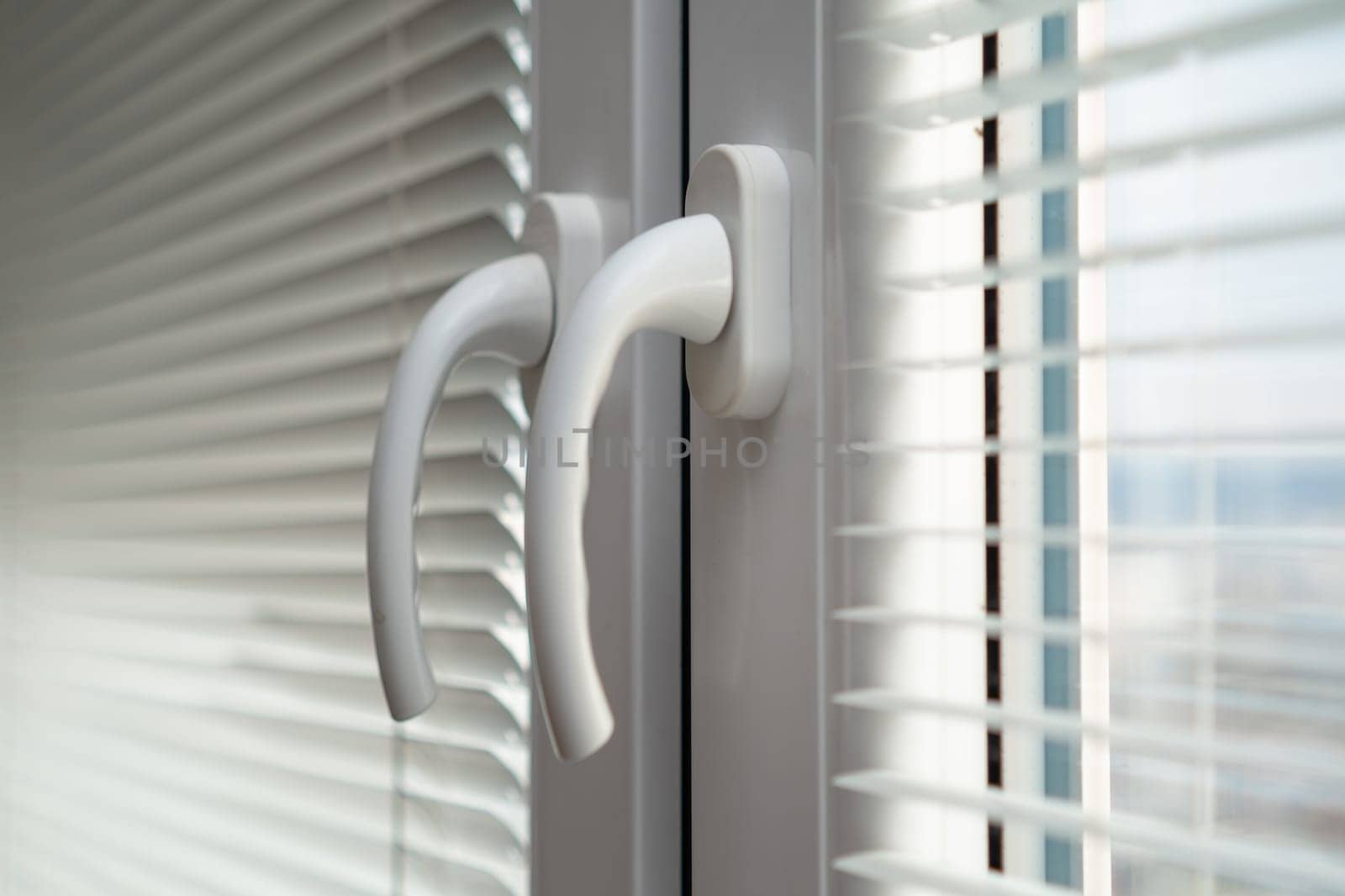 Handles of closed white plastic window with blinds.