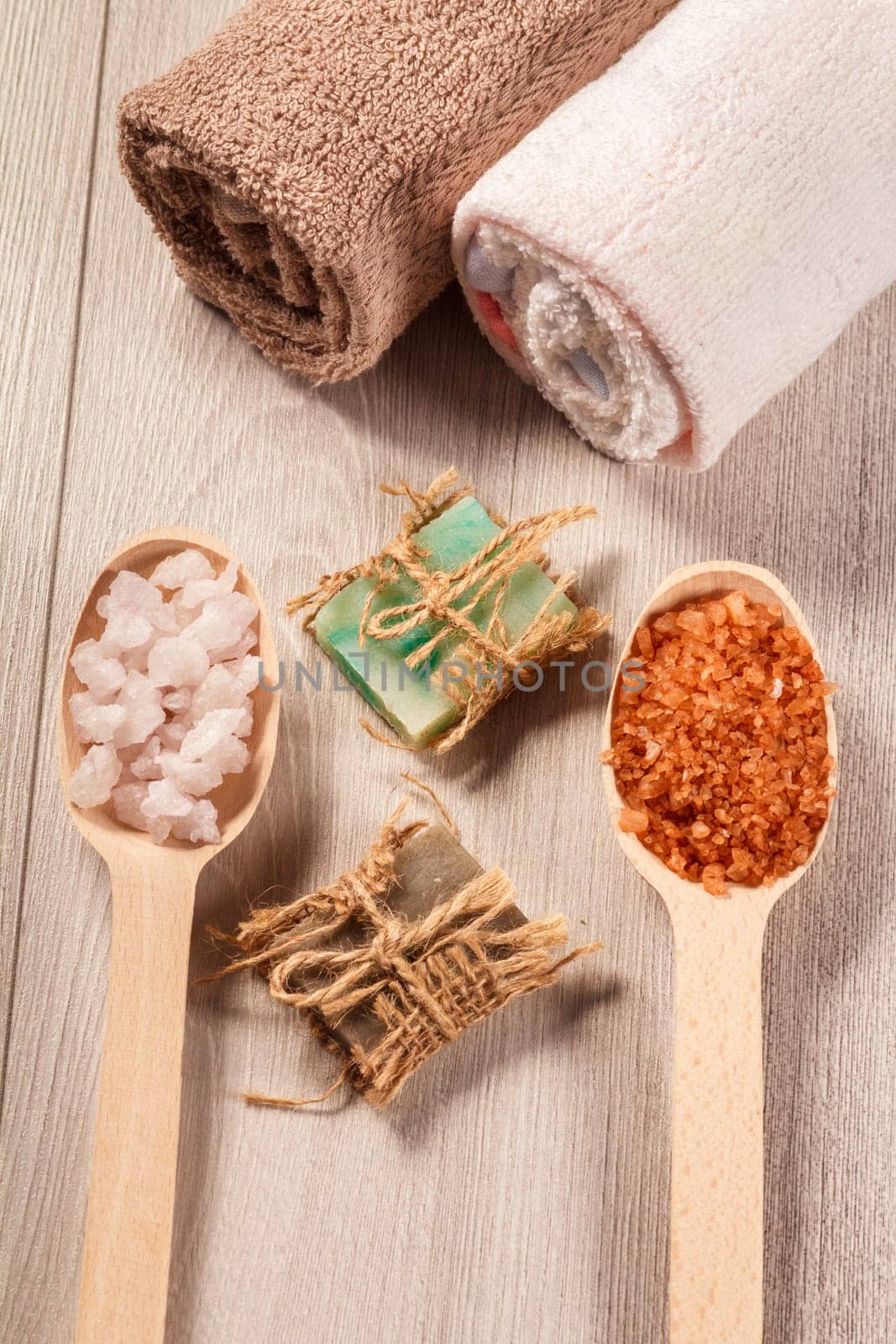 Wooden spoons with white and brown sea salt and handmade soap for bathroom procedures with towels on the background. Spa products and accessories