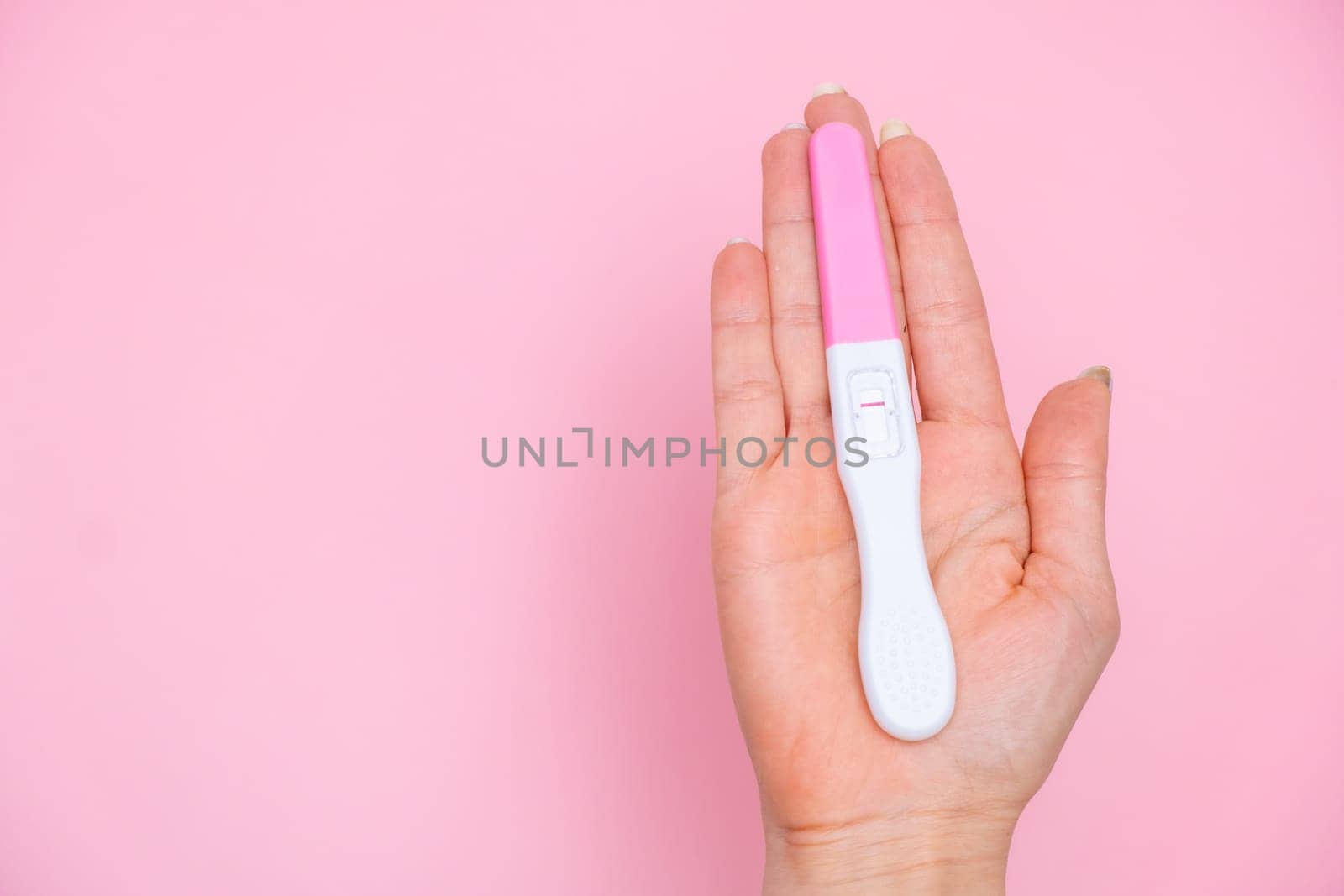 Female hand holding a negative pregnancy test on the pink background with copy space.