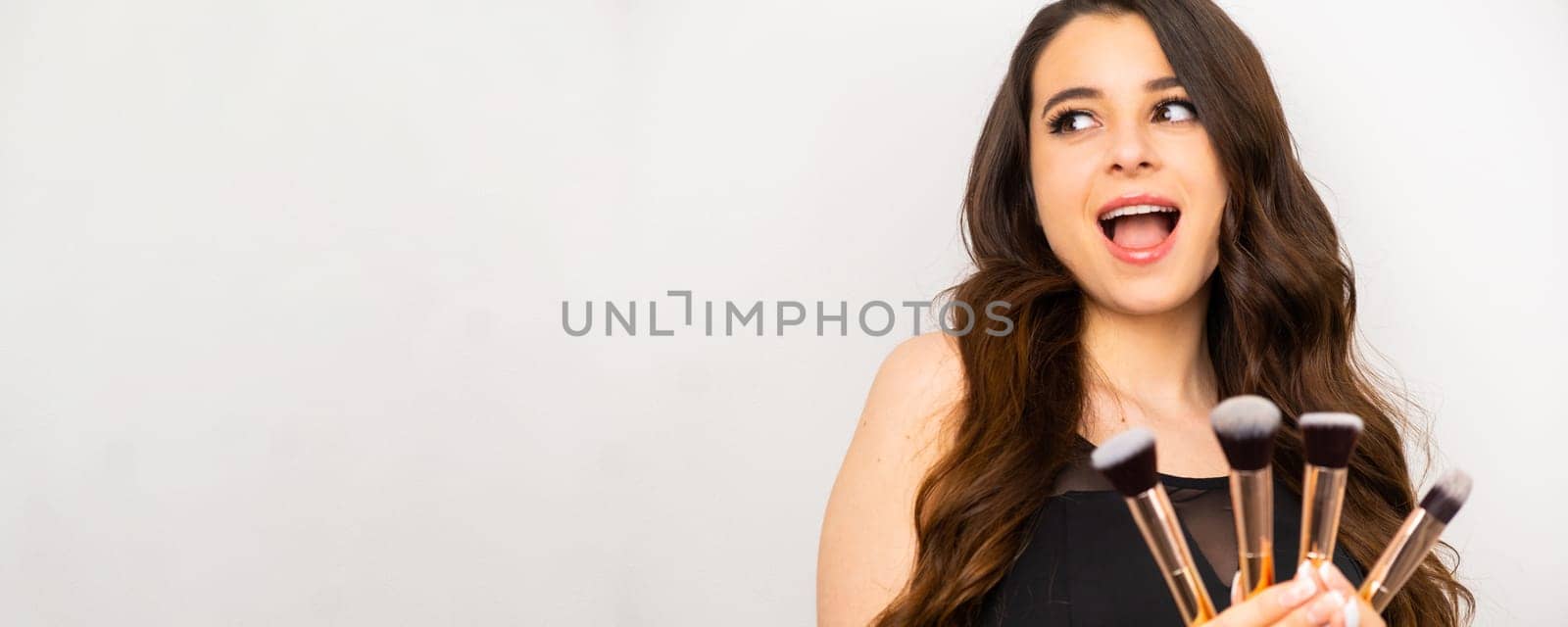 Beauty portrait of a joyful woman holding makeup brushes on a white background, banner