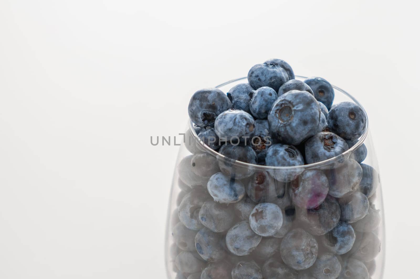 Glass bowl with blueberries on white table, close up.