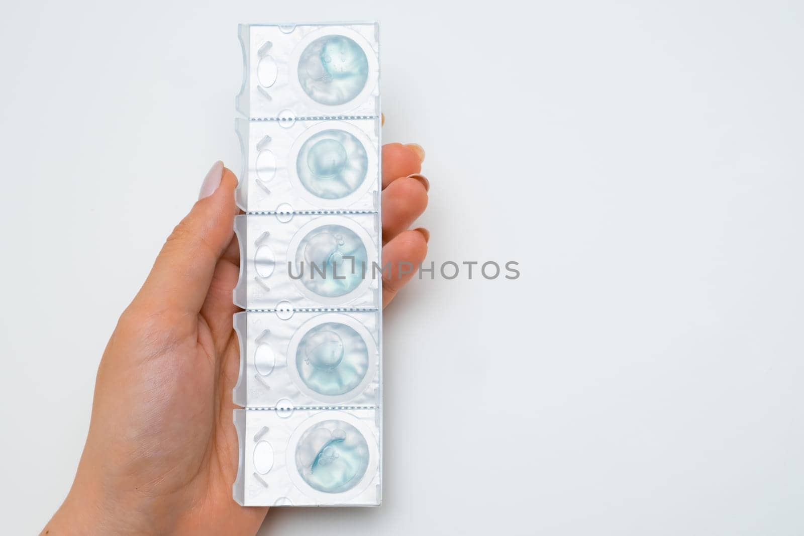 Contact lenses in blister with a solution in womans hands on the white background with copy space.