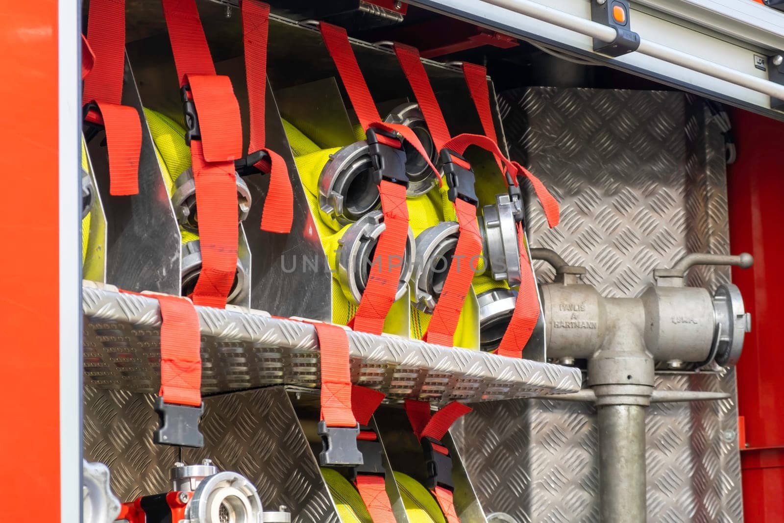 Rolled yellow hoses fastened in cells by belts with clamps in open fire truck metal body at contemporary station close view