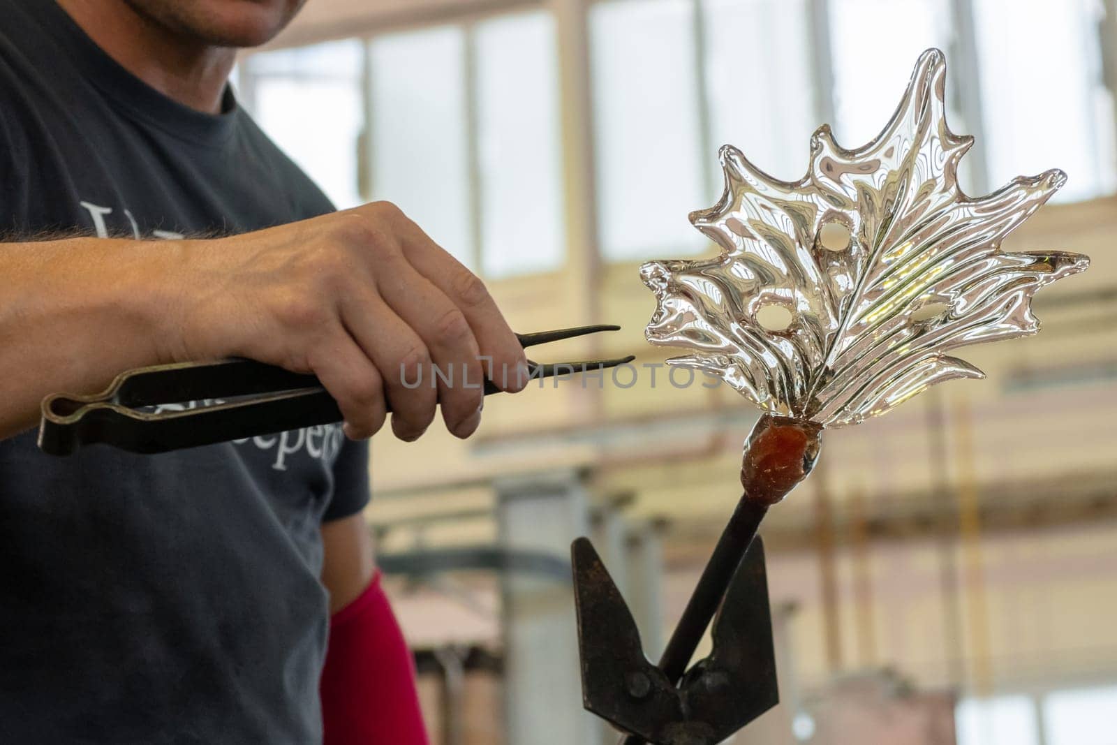 Close up man makes a leaf from the glass for vase or chandelier using tongs and blowpipe.