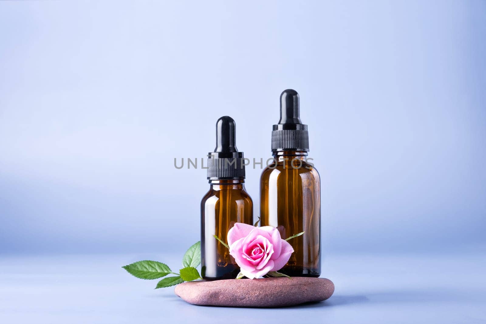 Two glass brown bottles with a pipette for a cosmetic product with a rose on the stones. Natural cosmetics for face and body skin care. Selective focus.