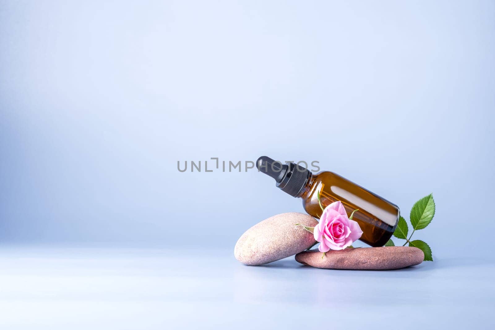 Glass brown bottle with a pipette for a cosmetic product with a rose on stones. Natural cosmetics for face and body skin care. Selective focus. Copy space.