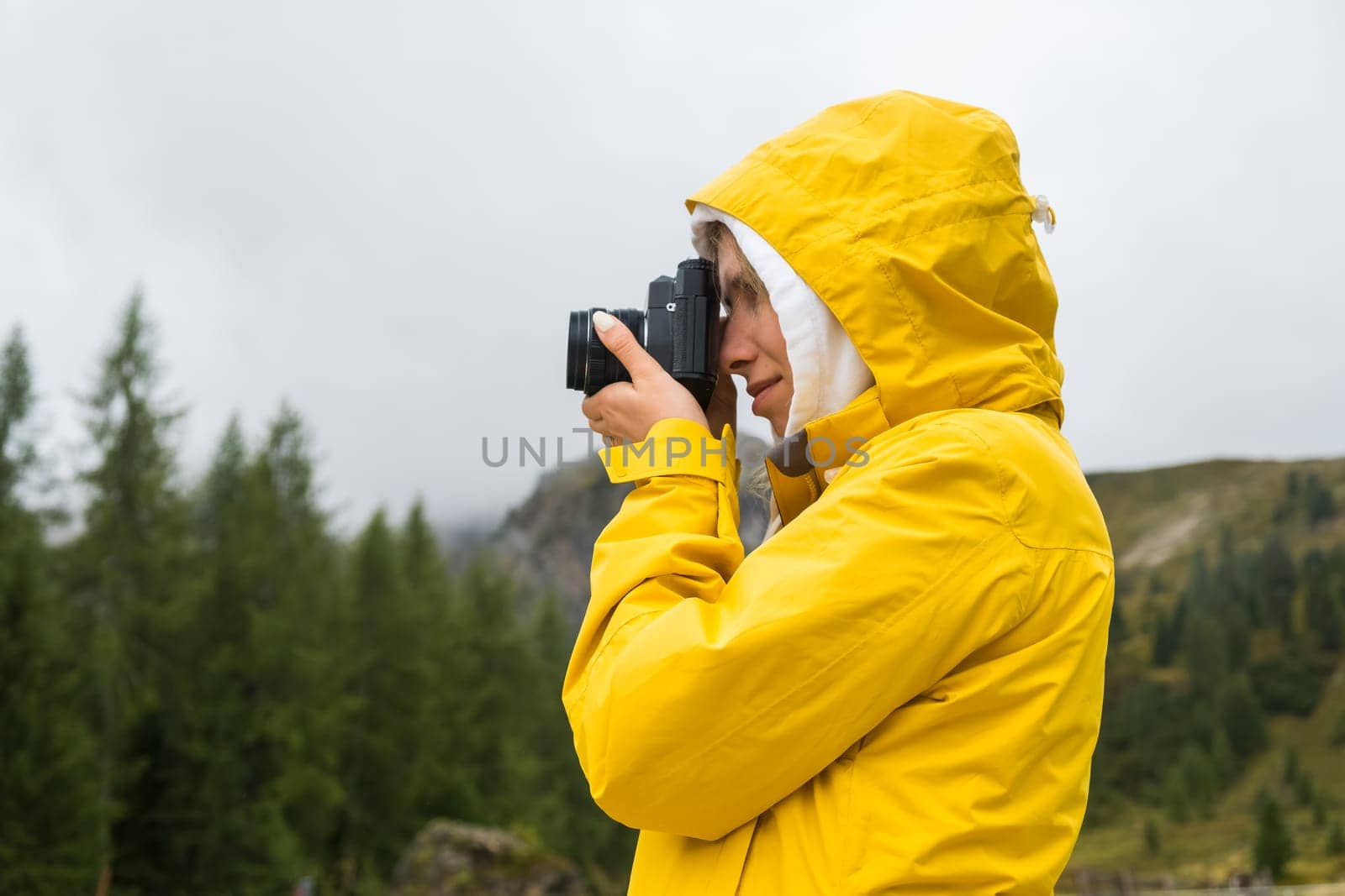 Lady in yellow jacket makes photos of meadows of Alps. Young woman tourist captures moments with camera and explores foggy hillside in mountains