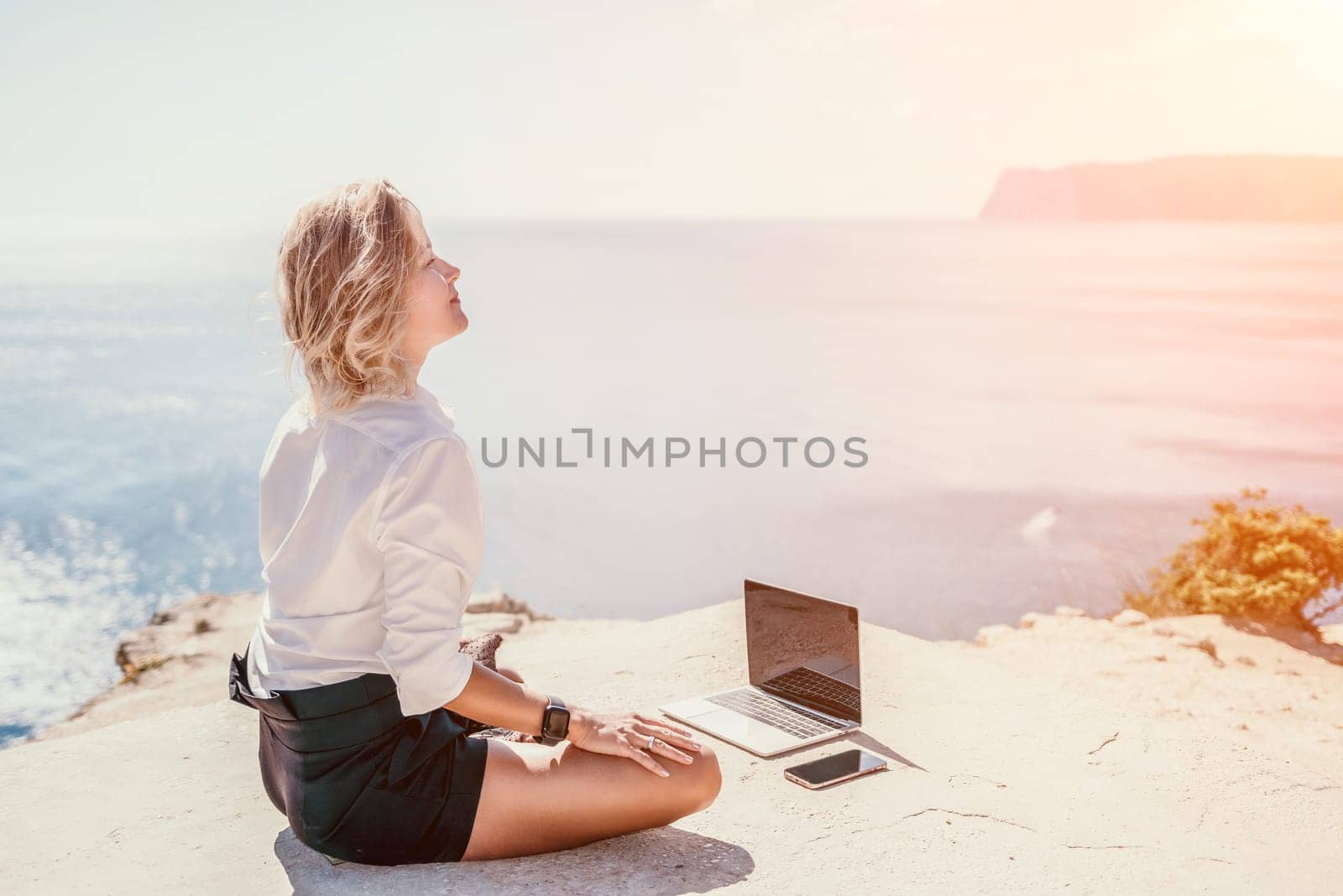 Happy girl doing yoga with laptop working at the beach. beautiful and calm business woman sitting with a laptop in a summer cafe in the lotus position meditating and relaxing. freelance girl remote work beach paradise