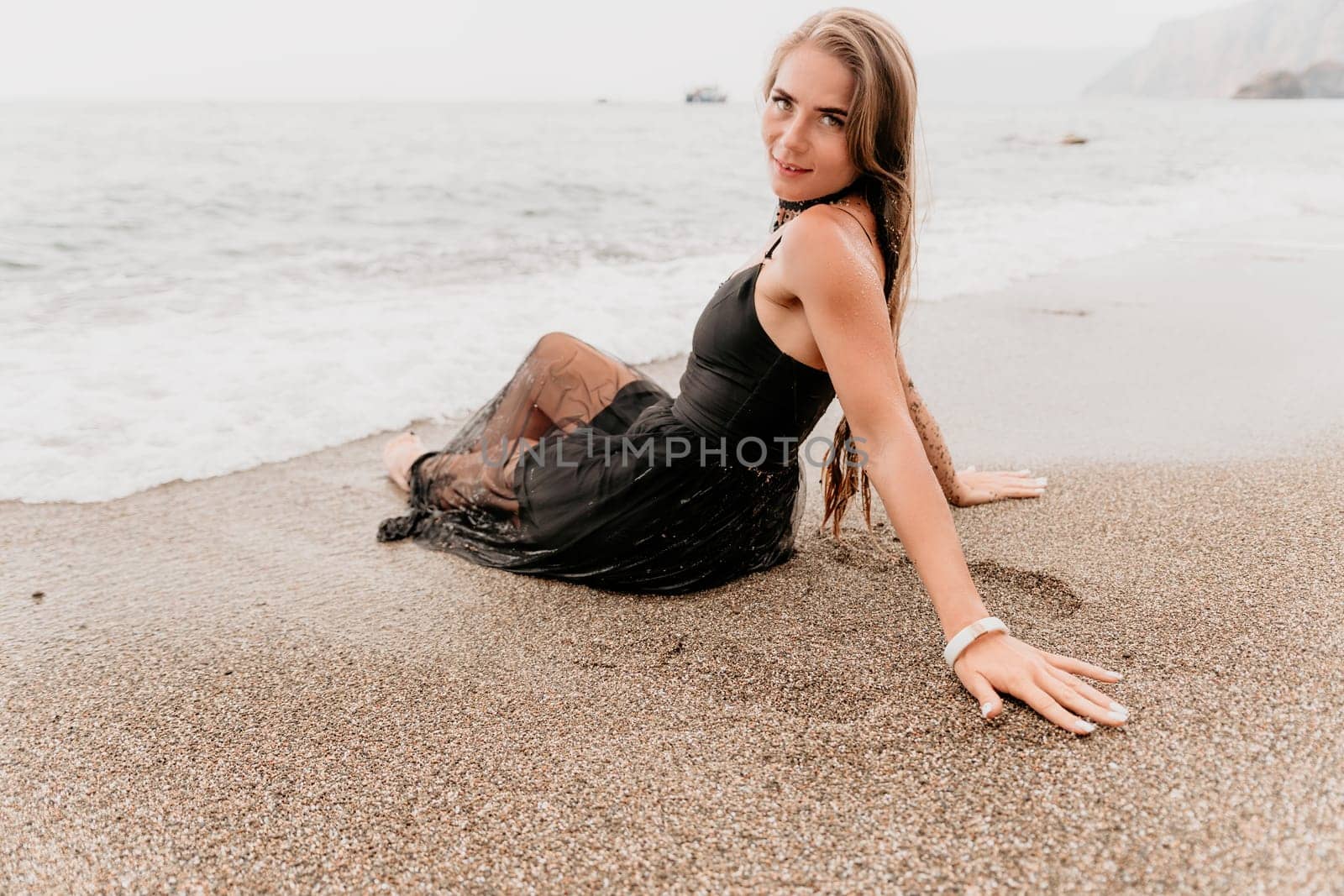 Woman travel sea. Young Happy woman in a long red dress posing on a beach near the sea on background of volcanic rocks, like in Iceland, sharing travel adventure journey