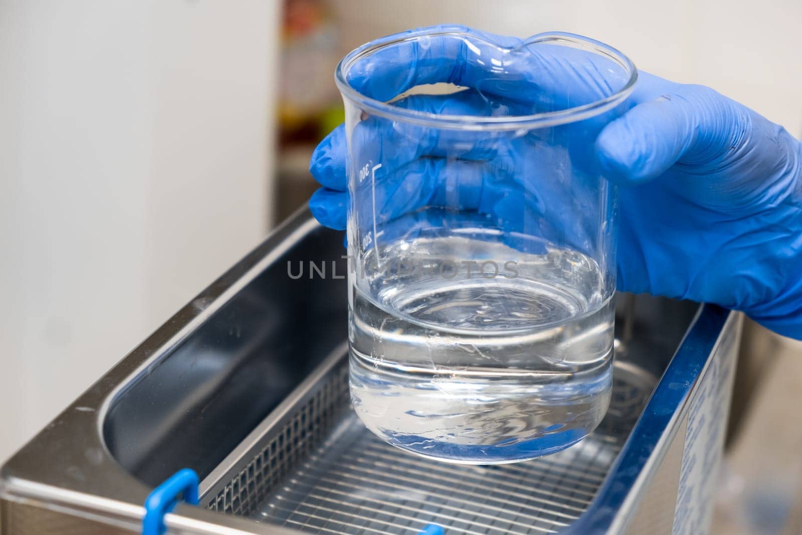 Scientist in blue rubber puts a beaker for dissolving or cleaning into an ultrasound bath. Clinical, toxicological and forensic analysis.