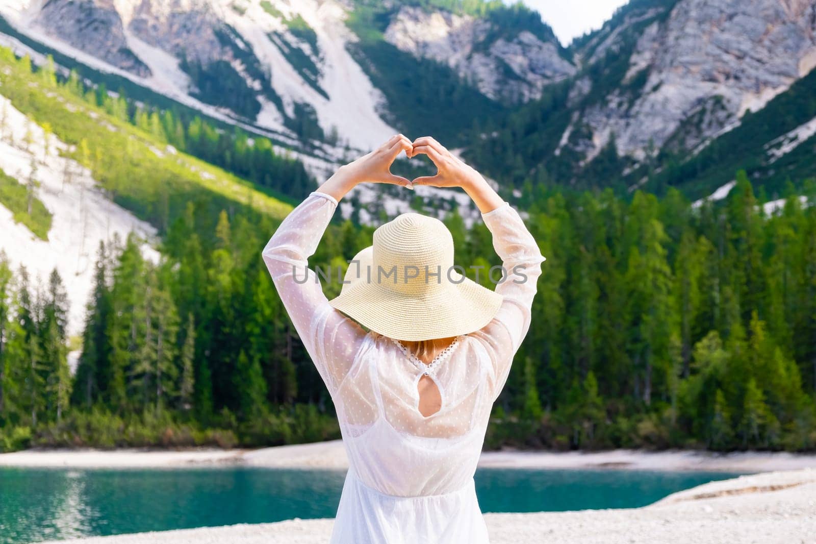 Blonde hair woman shows the heart with her hands on the background of the Dolomites and Lake Braies.