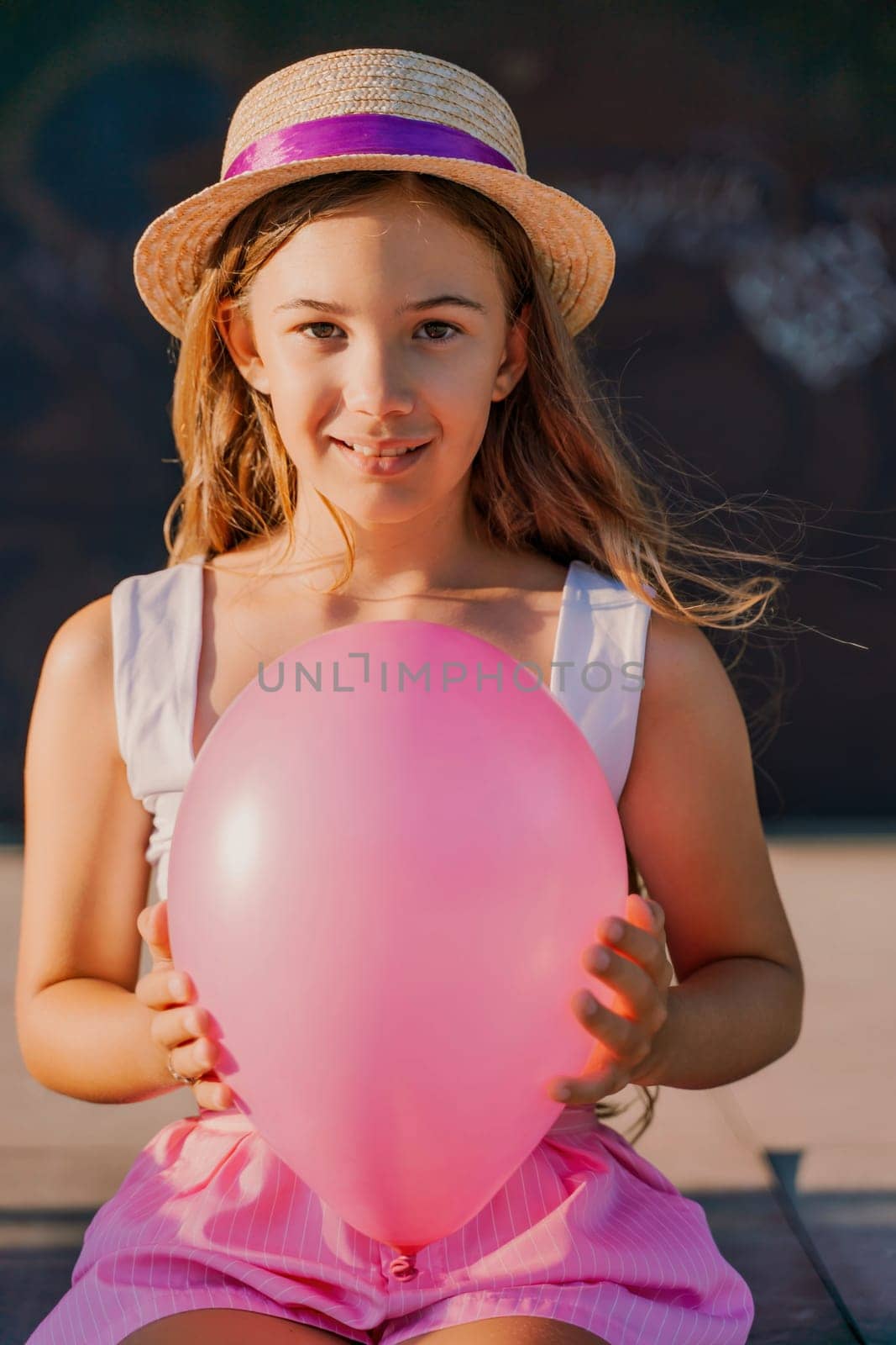 Portrait of a girl in a hat with a pink balloon. She is dressed in pink clothes and her hair is long and loose