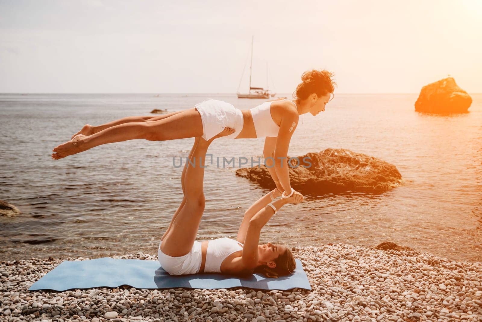 Woman sea yoga. Two Happy women meditating in yoga pose on the beach, ocean and rock mountains. Motivation and inspirational fit and exercising. Healthy lifestyle outdoors in nature, fitness concept. by panophotograph