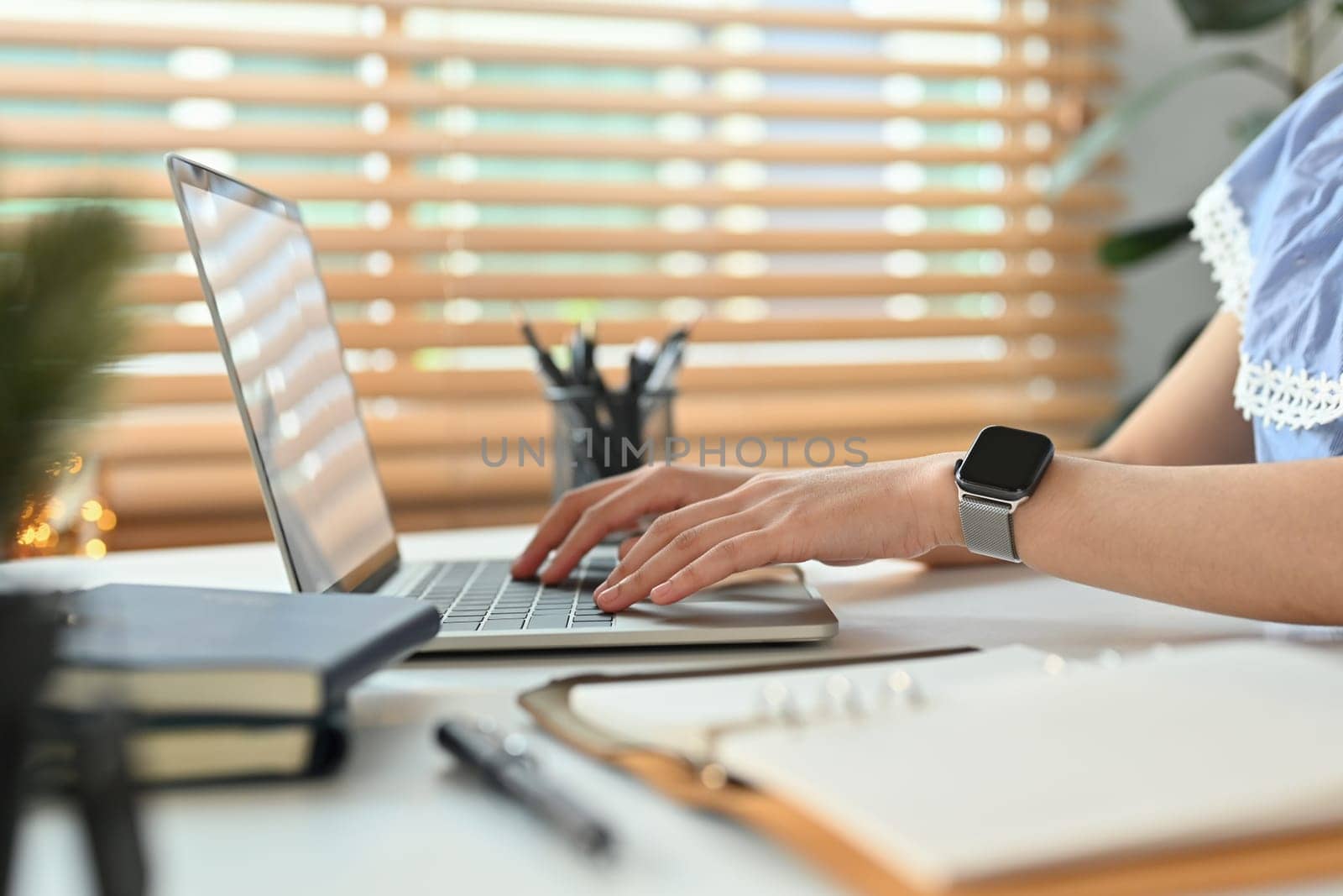 Side view of modern young woman hands wearing smartwatch typing on laptop computer by prathanchorruangsak