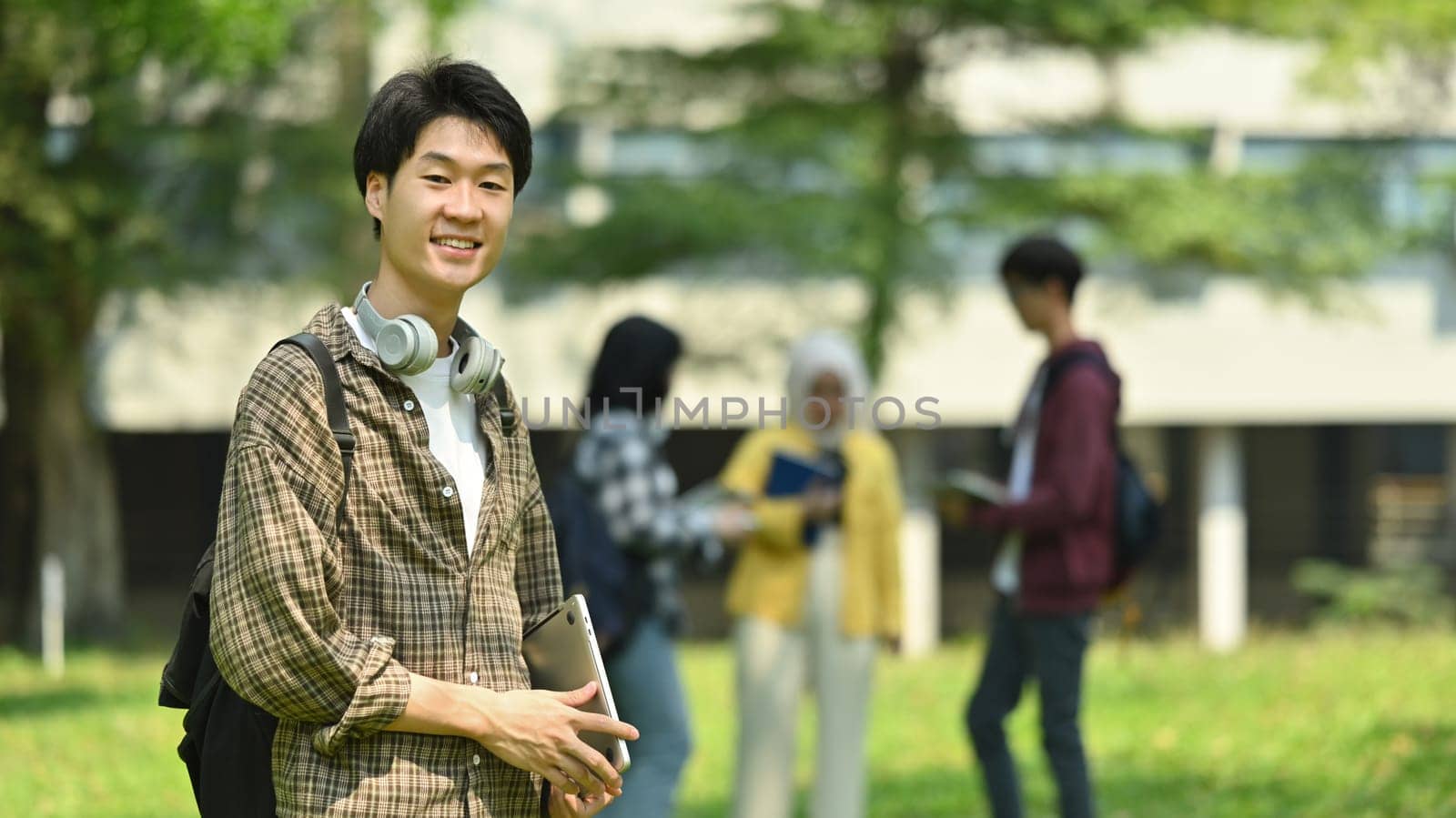 Portrait of asian male student with backpack standing outdoors by modern campus building.