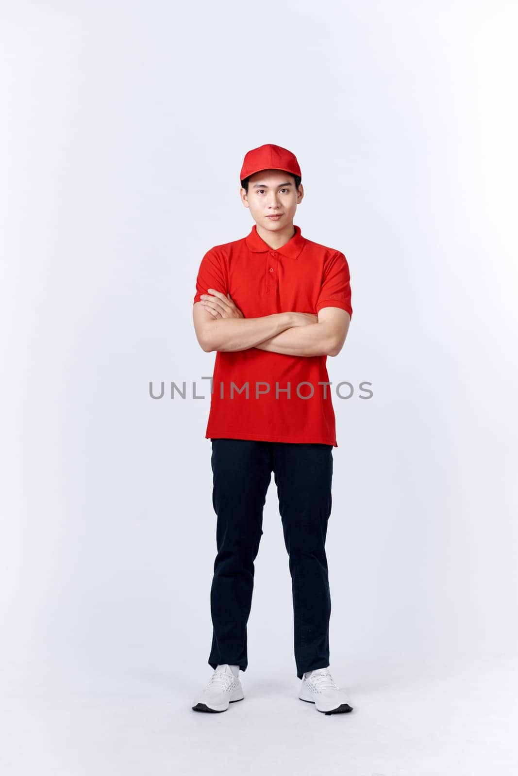 Smiling delivery man in red uniform standing with arm crossed - isolated on white background by makidotvn