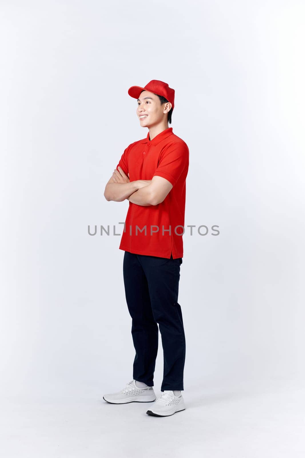 Smiling delivery man in red uniform standing with arm crossed - isolated on white background by makidotvn