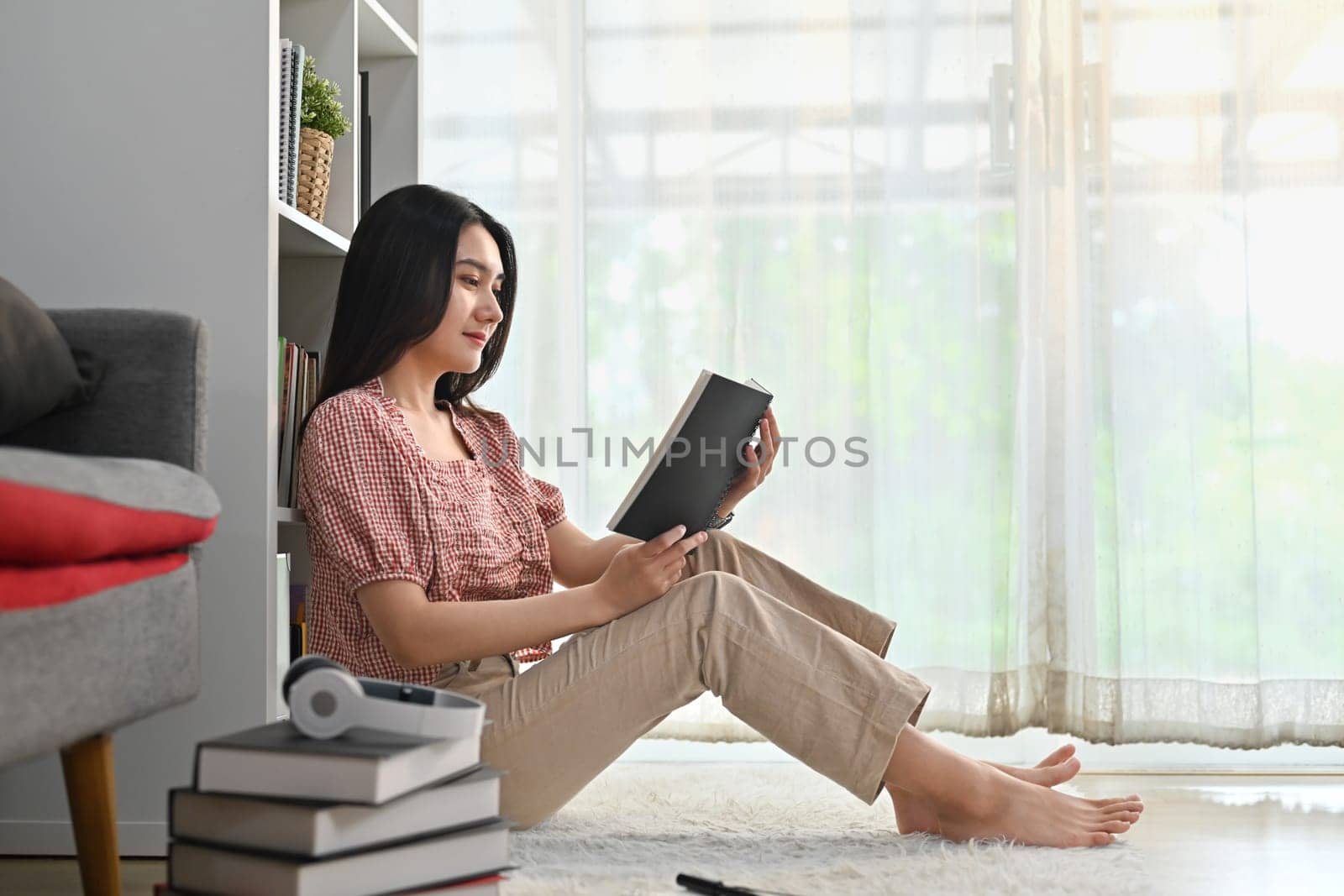 Beautiful woman sitting floor in living room and reading a book, spending leisure weekend time at home.