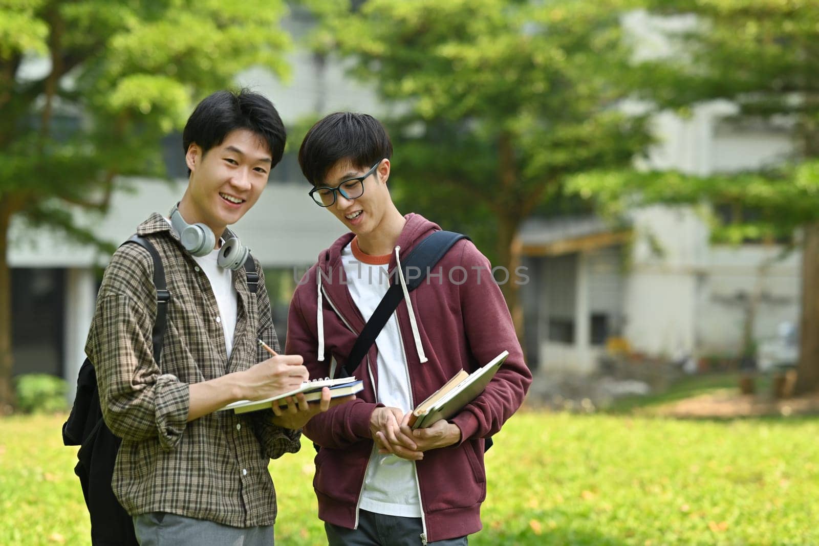 Two friendly students are talking to each other after classes while walking in university campus outdoors. Youth lifestyle concept.