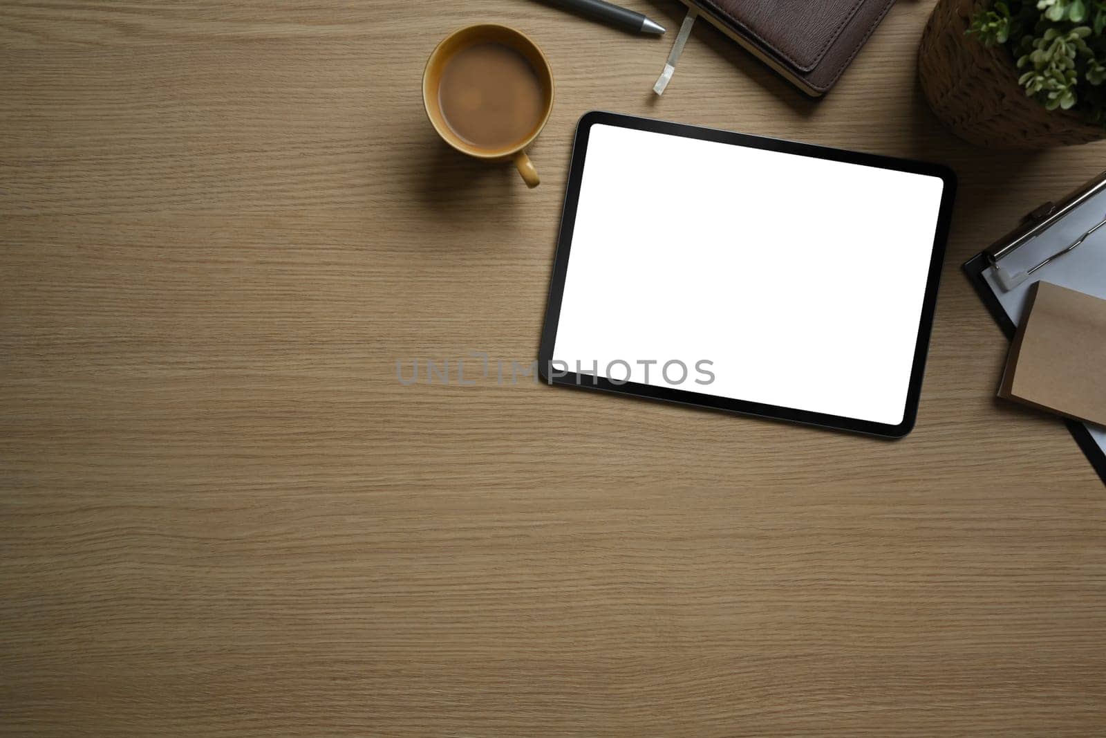 Flat lay, top view of simple workspace with digital tablet, cup of coffee and notebook on wooden table by prathanchorruangsak