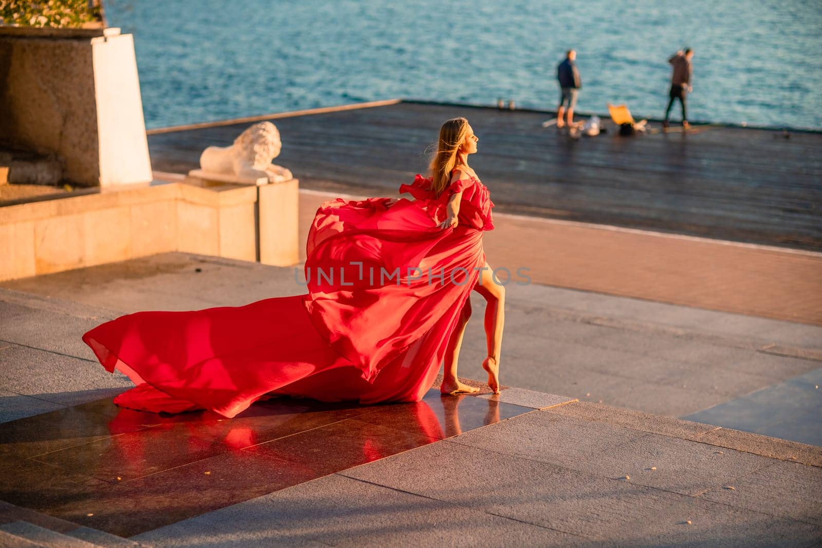 Sunrise red dress. A woman in a long red dress against the backdrop of sunrise, bright golden light of the sun's rays. The concept of femininity, harmony