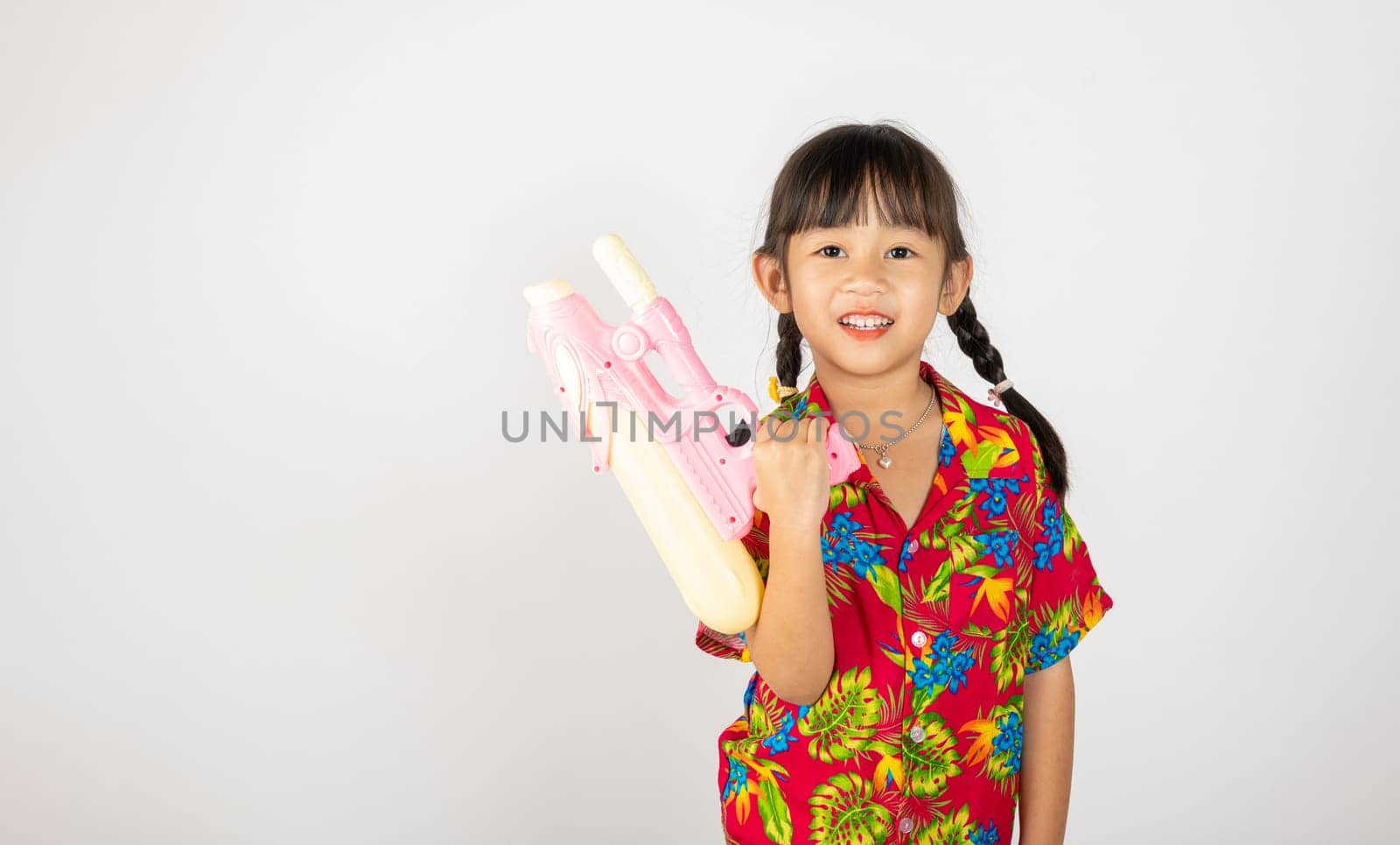 Happy Songkran Day, Asian kid girl with floral shirt hold water gun, Thai child funny hold toy water pistol and smile, isolated on white background, Thailand Songkran festival national culture concept