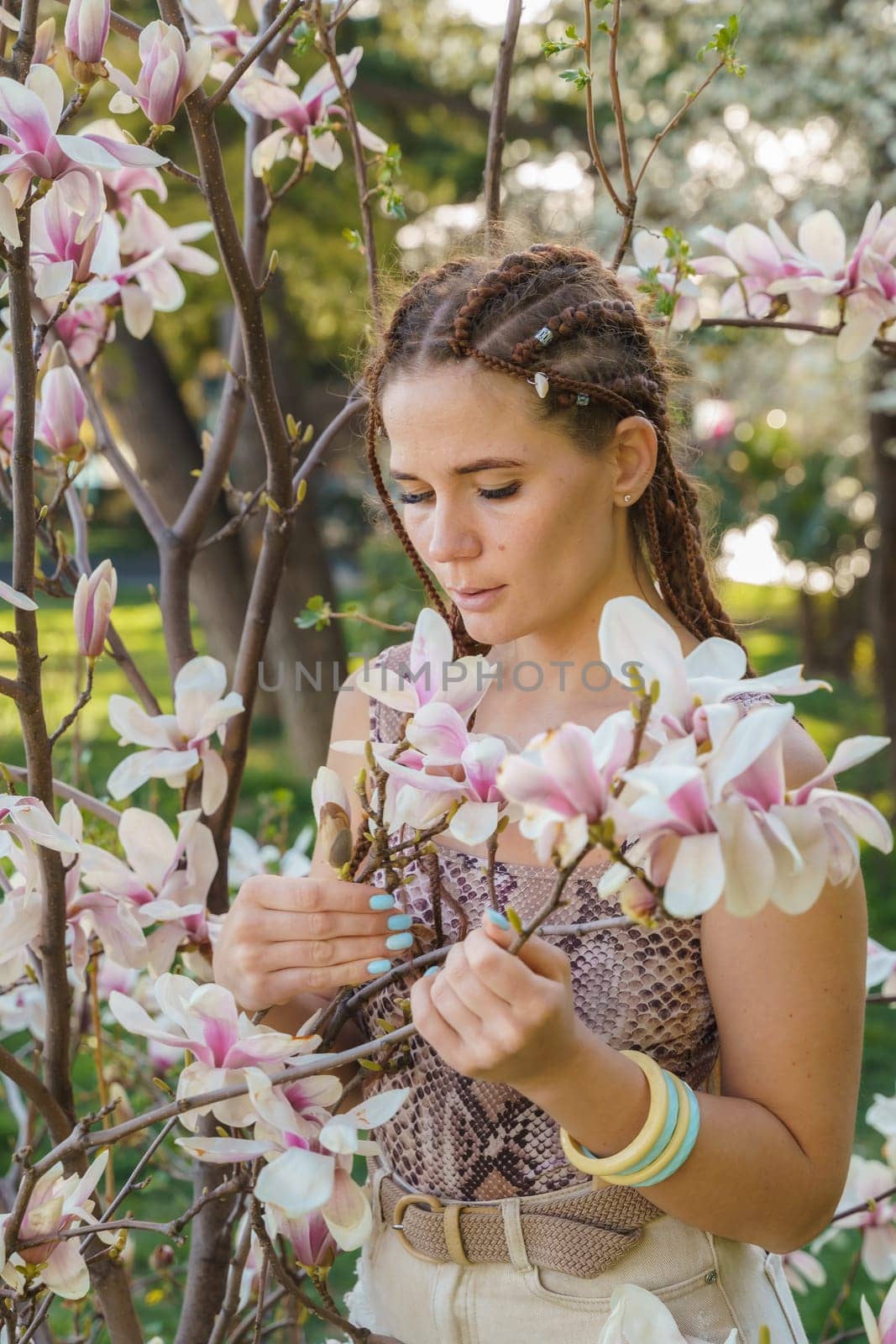 Magnolia flowers. Happy woman enjoys by blooming magnolia tree and sniffs it flowers with closed eyes in spring garden. Portrait. by Matiunina