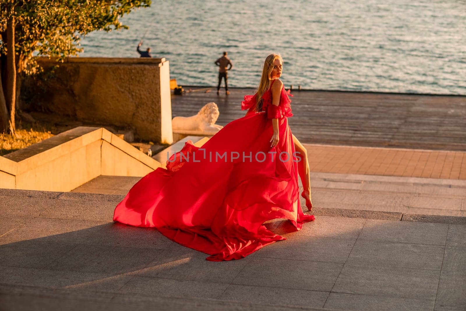 Sunrise red dress. A woman in a long red dress against the backdrop of sunrise, bright golden light of the sun's rays. The concept of femininity, harmony