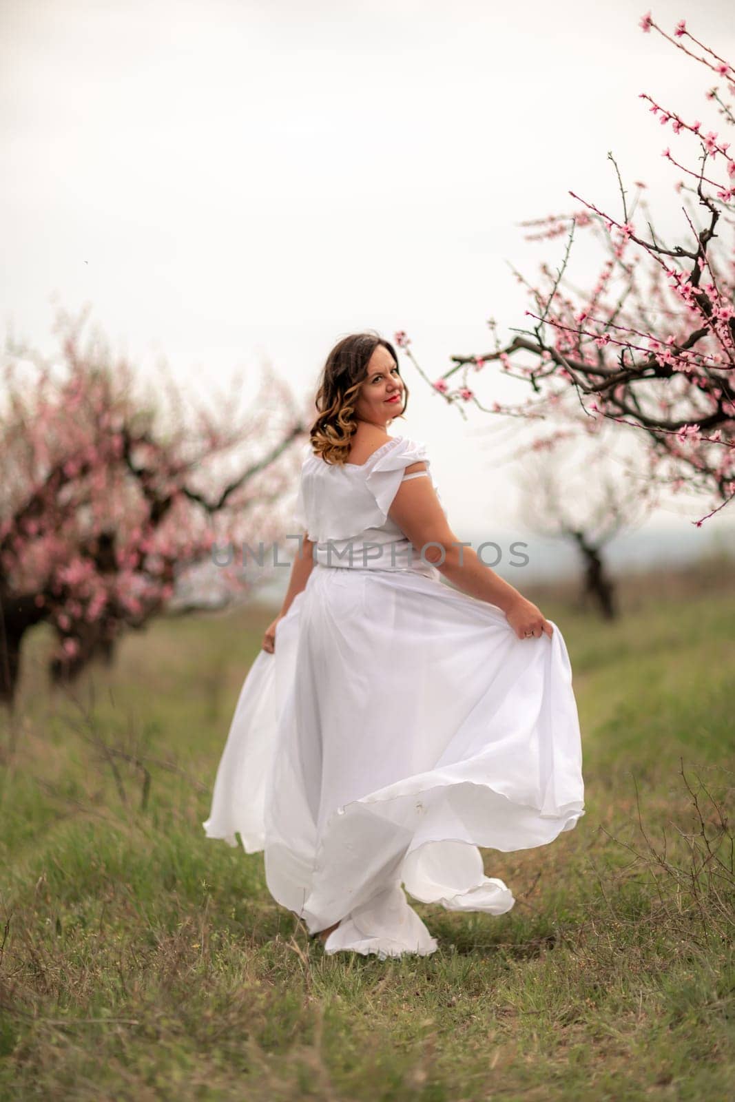 Woman peach blossom. Happy woman in white dress walking in the garden of blossoming peach trees in spring by Matiunina