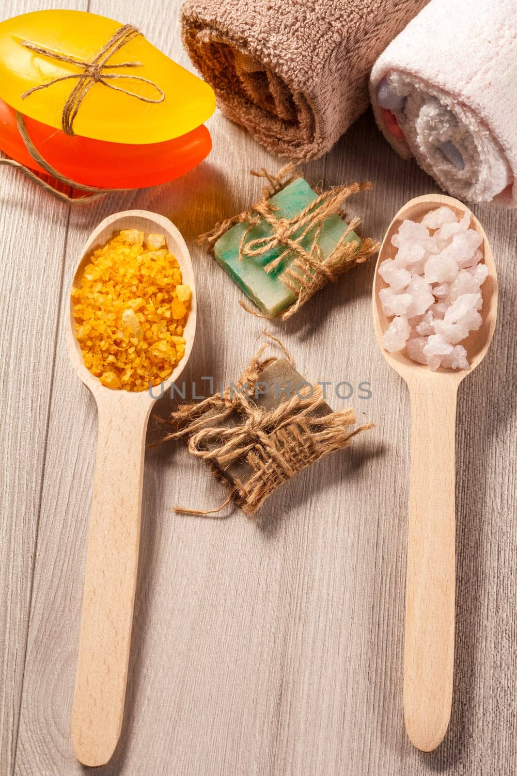 Wooden spoons with yellow and white sea salt and handmade soap for bathroom procedures with towels on the background. Spa products and accessories