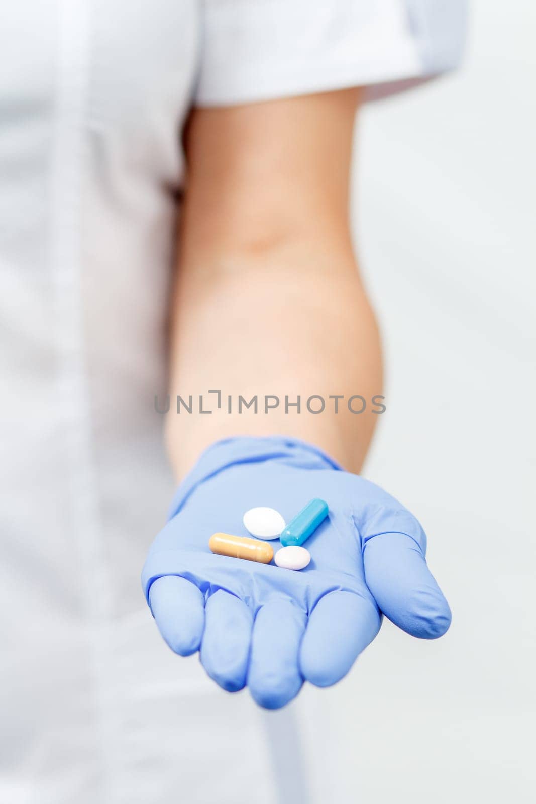 Hand of female doctor in blue glove with pile of pills of different color. Selective focus on pills