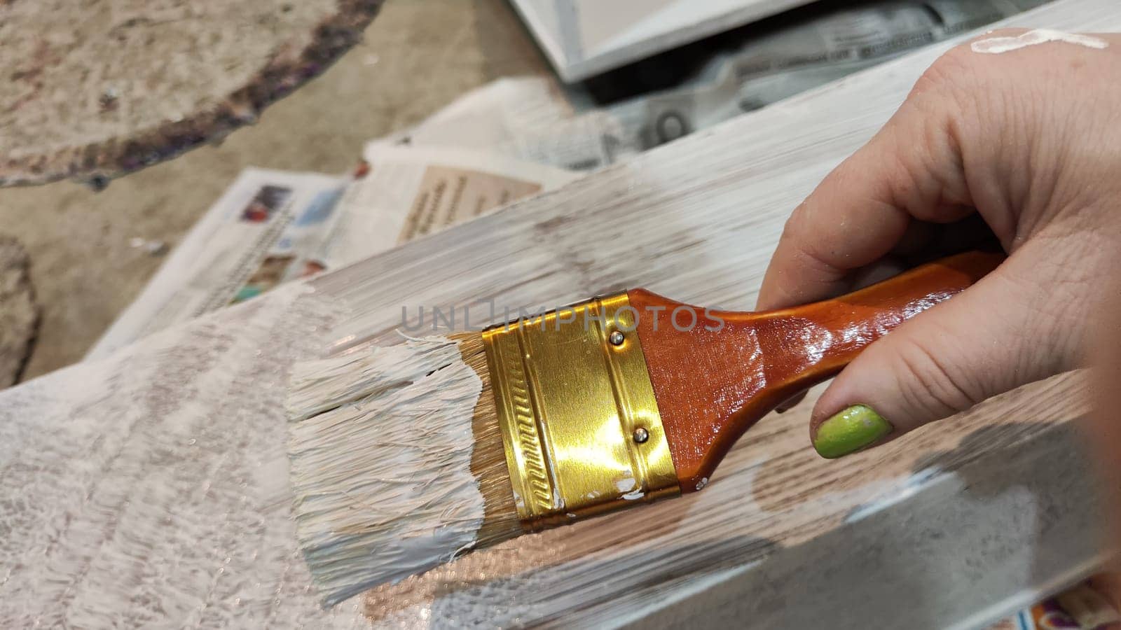 Woman hand painting on wooden boards with Brush full of white paint. Painting of new wood board or furniture and old newspaper on background. Partial focus