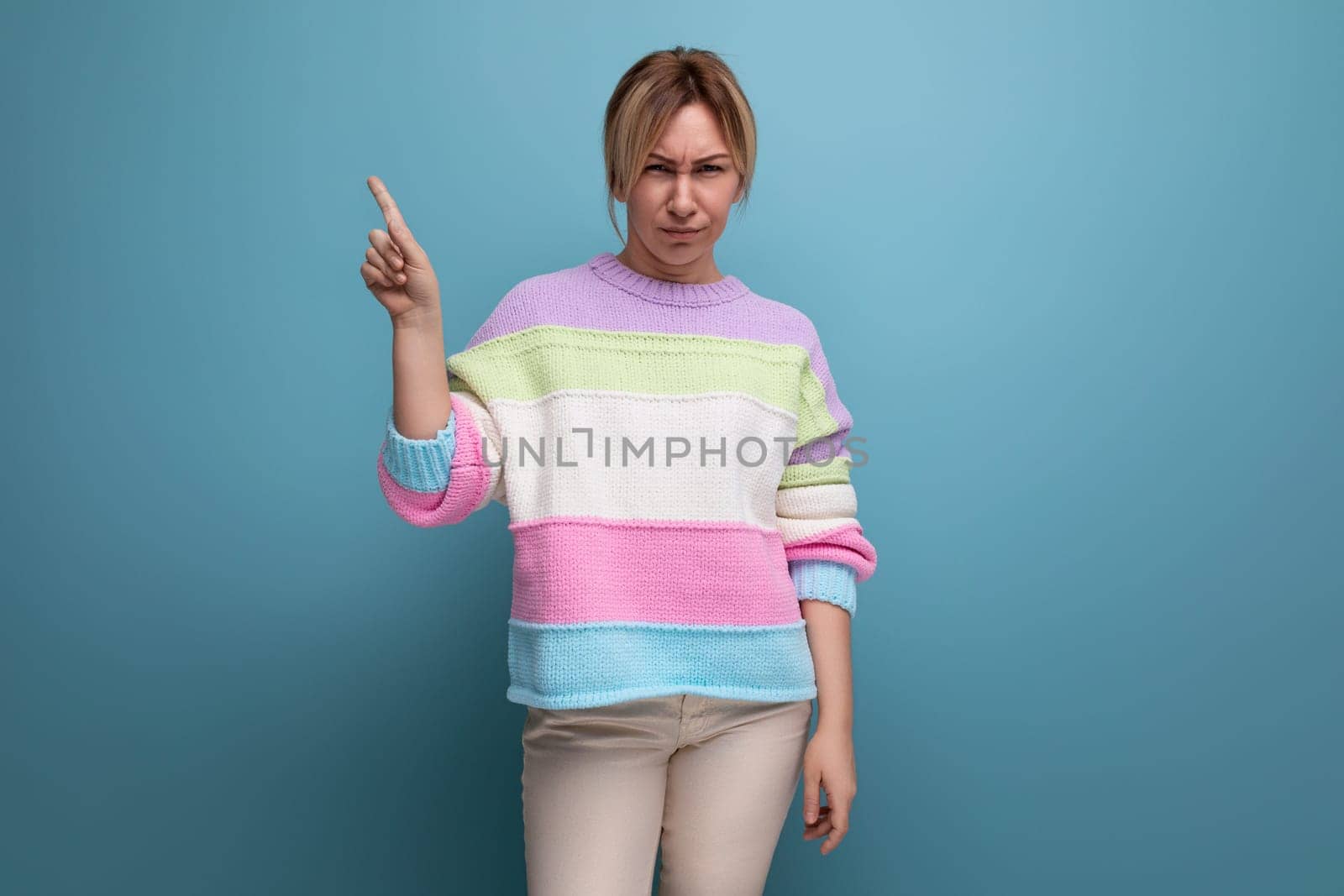 neat cute blond woman in a casual look shows her hands at the wall with copy space on a blue background.