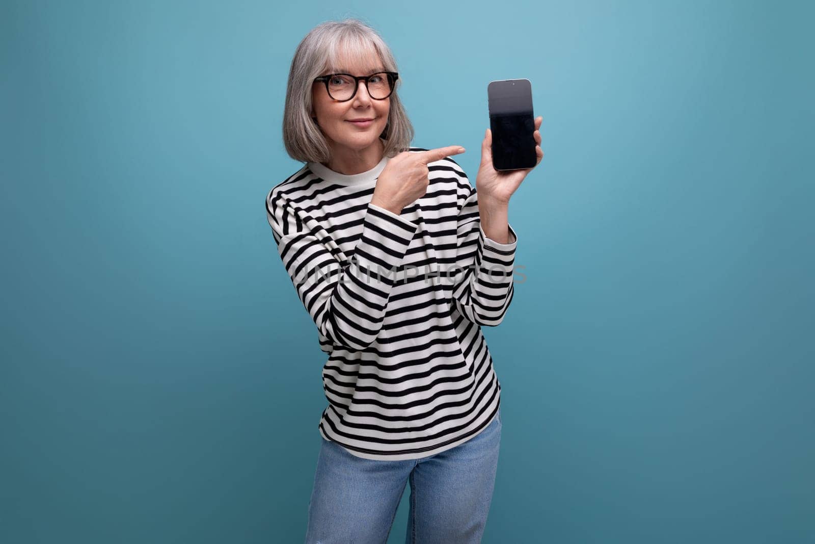 portrait of a fashionable 60s old lady holding a smartphone with a mockup on a bright background with copy space by TRMK