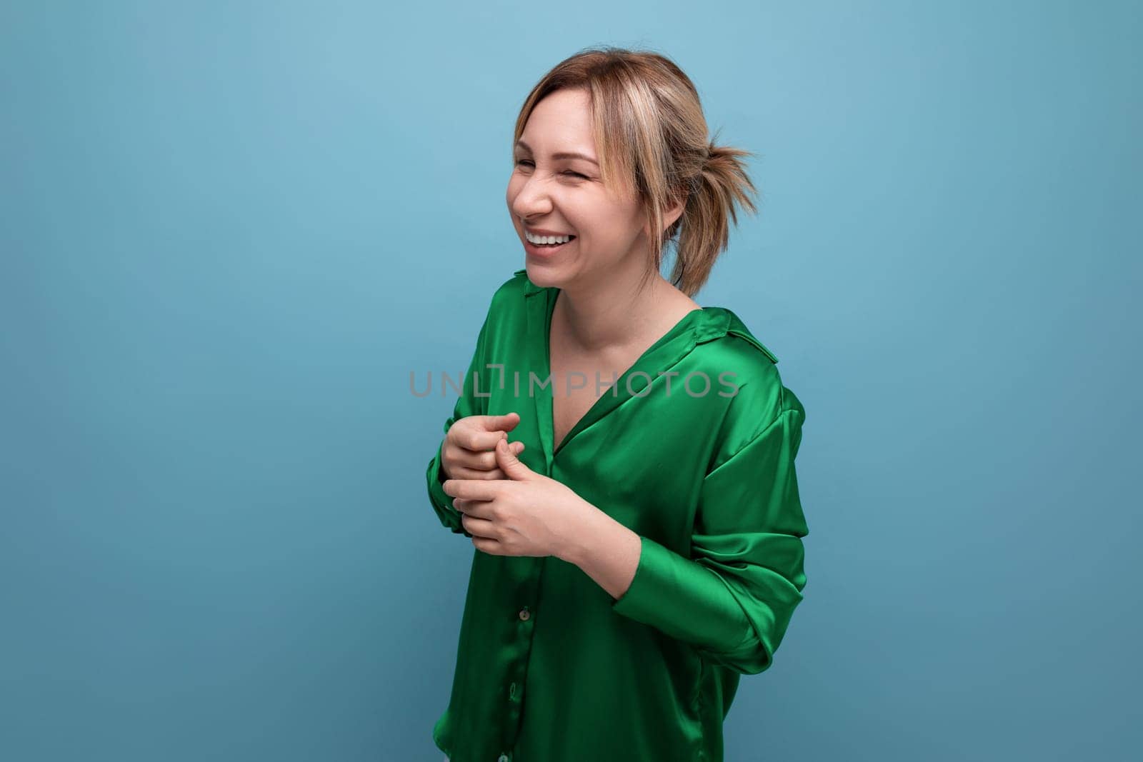 attractive blond young woman in green silk shirt laughing on blue background by TRMK