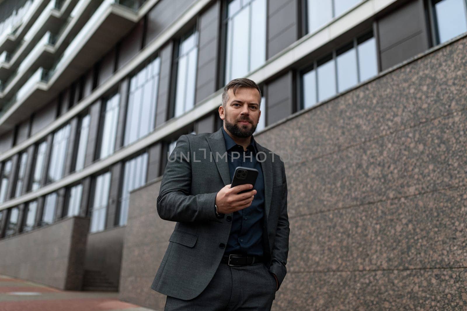 a businessman walks along the building on the street with a mobile phone in his hands.