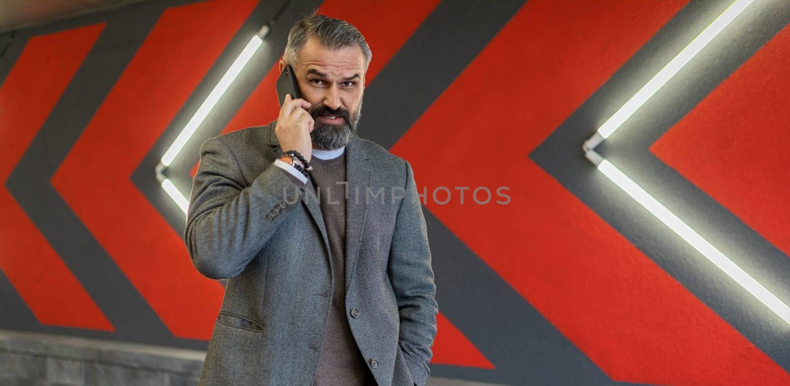 brutal adult male businessman speaks on a mobile phone against the background of a bright wall with red arrows.