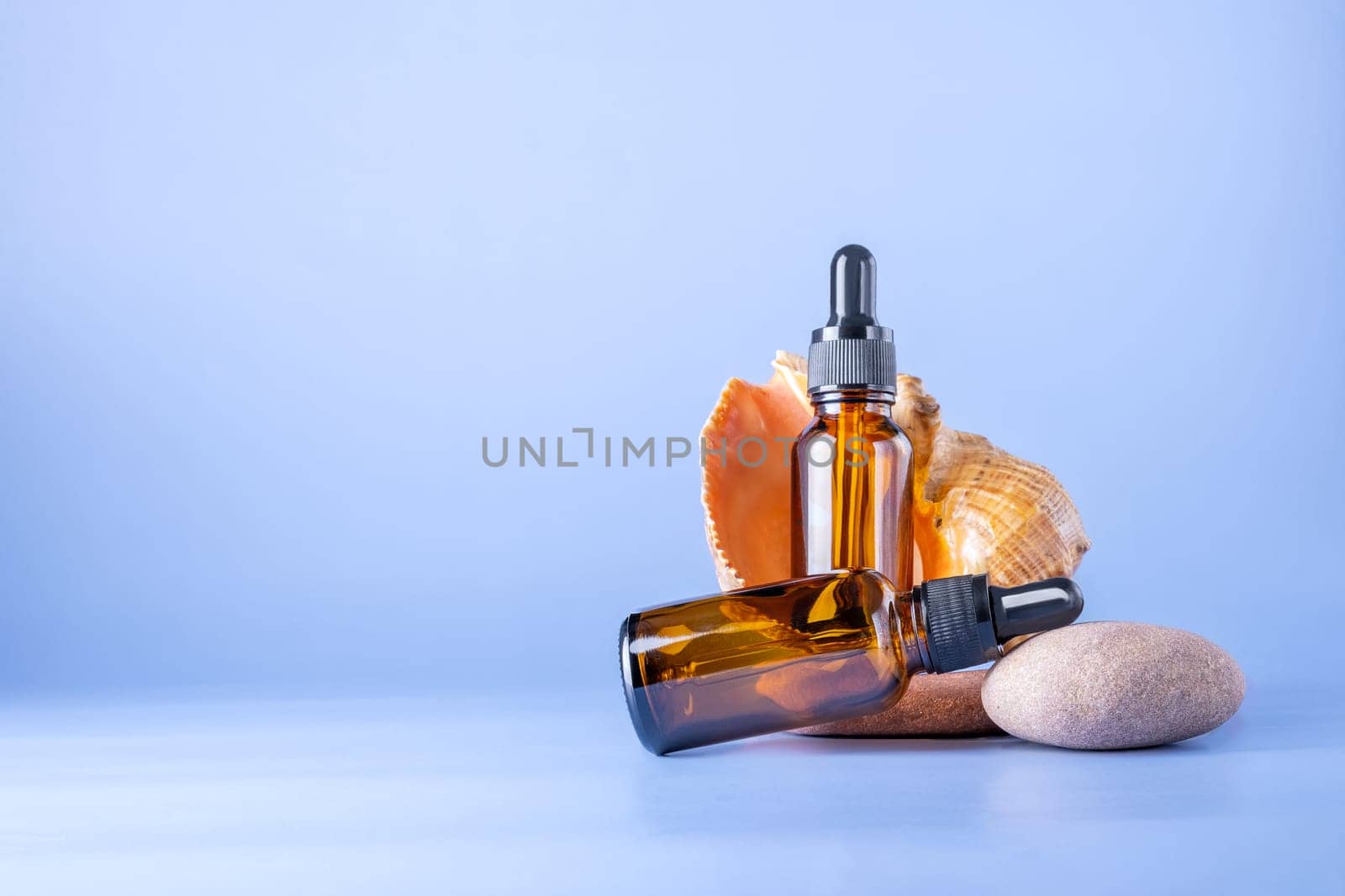 Two glass brown bottles with a pipette for a cosmetic product with a sea shell on stones. Natural cosmetics for face and body skin care. Selective focus. Place for text.