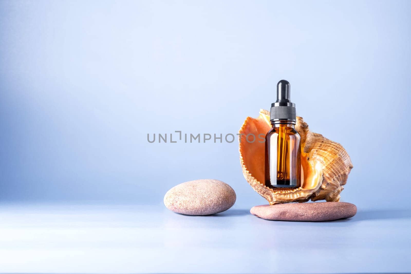 Glass brown bottle with a pipette for a cosmetic product with a sea shell on stones. Natural cosmetics for face and body skin care. Selective focus. Place for text.