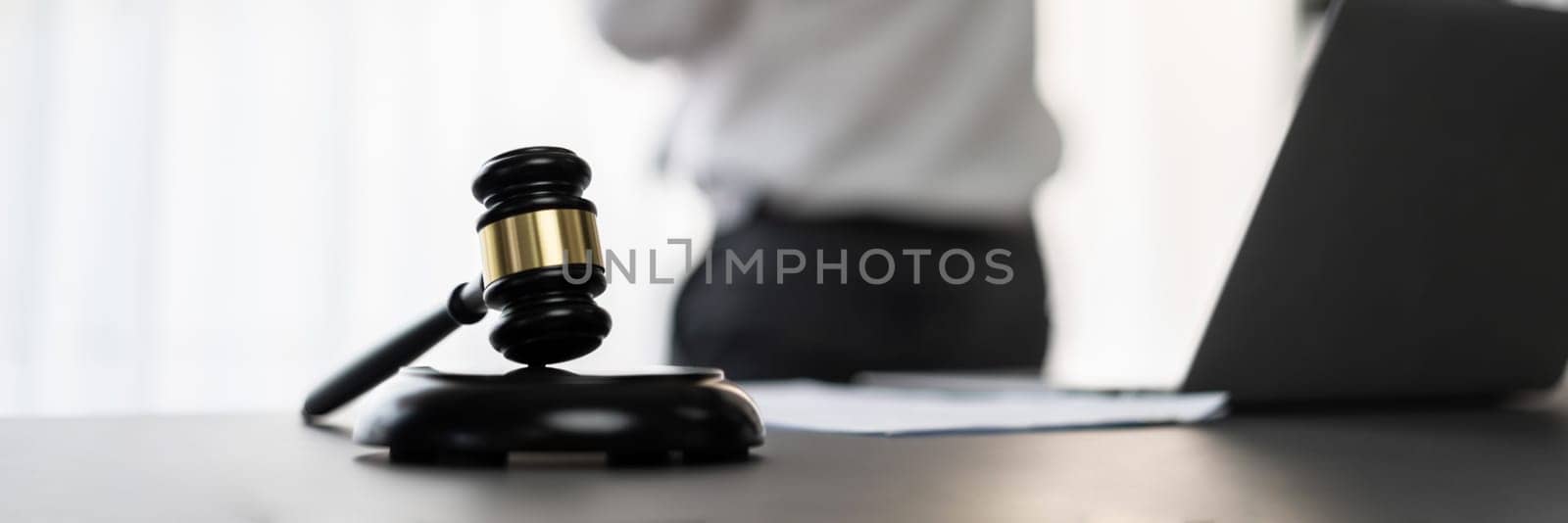 Focus wooden gavel hammer on blur background of lawyer working with legal document on desk at law firm office. Lawful hammer for righteous and equality judgment by lawmaker and attorney. Equilibrium