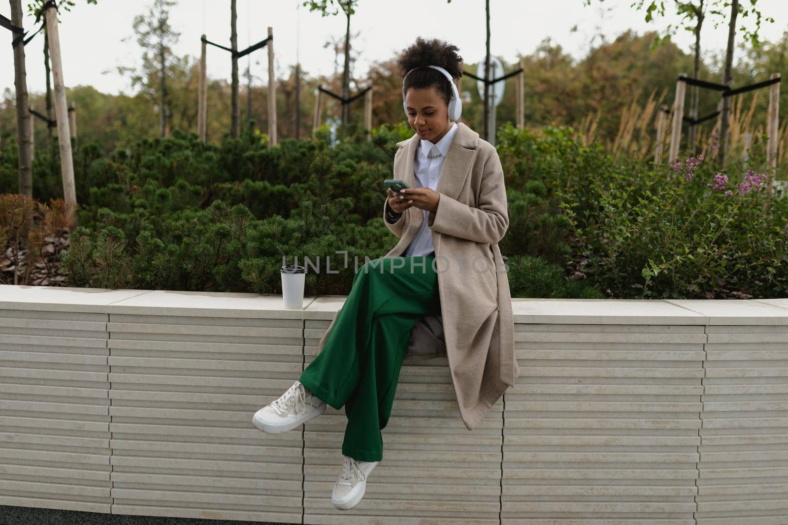 stylish african american girl student listening to music in headphones with a mobile phone in her hands outside.