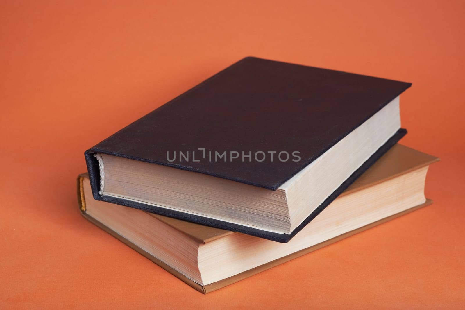 Two hardcover books on top of each other on a brown background. White and black book.