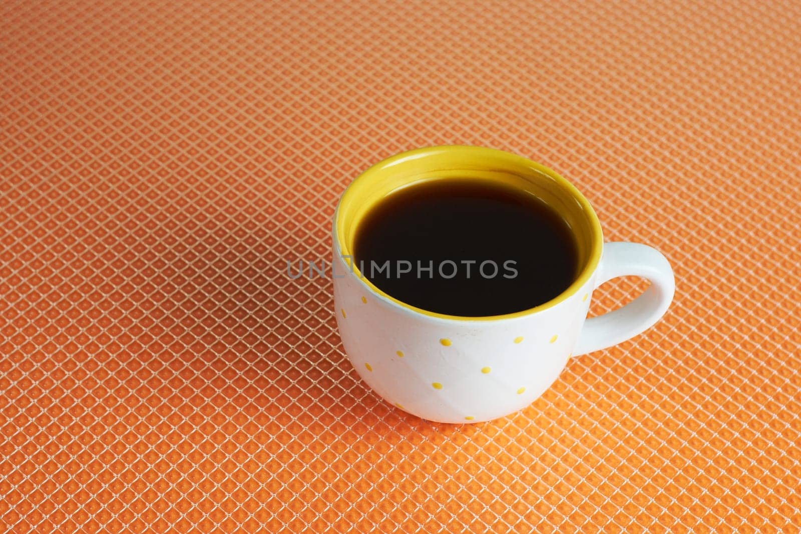 Flat view of a cup of dark hot coffee on an orange background with a space to copy