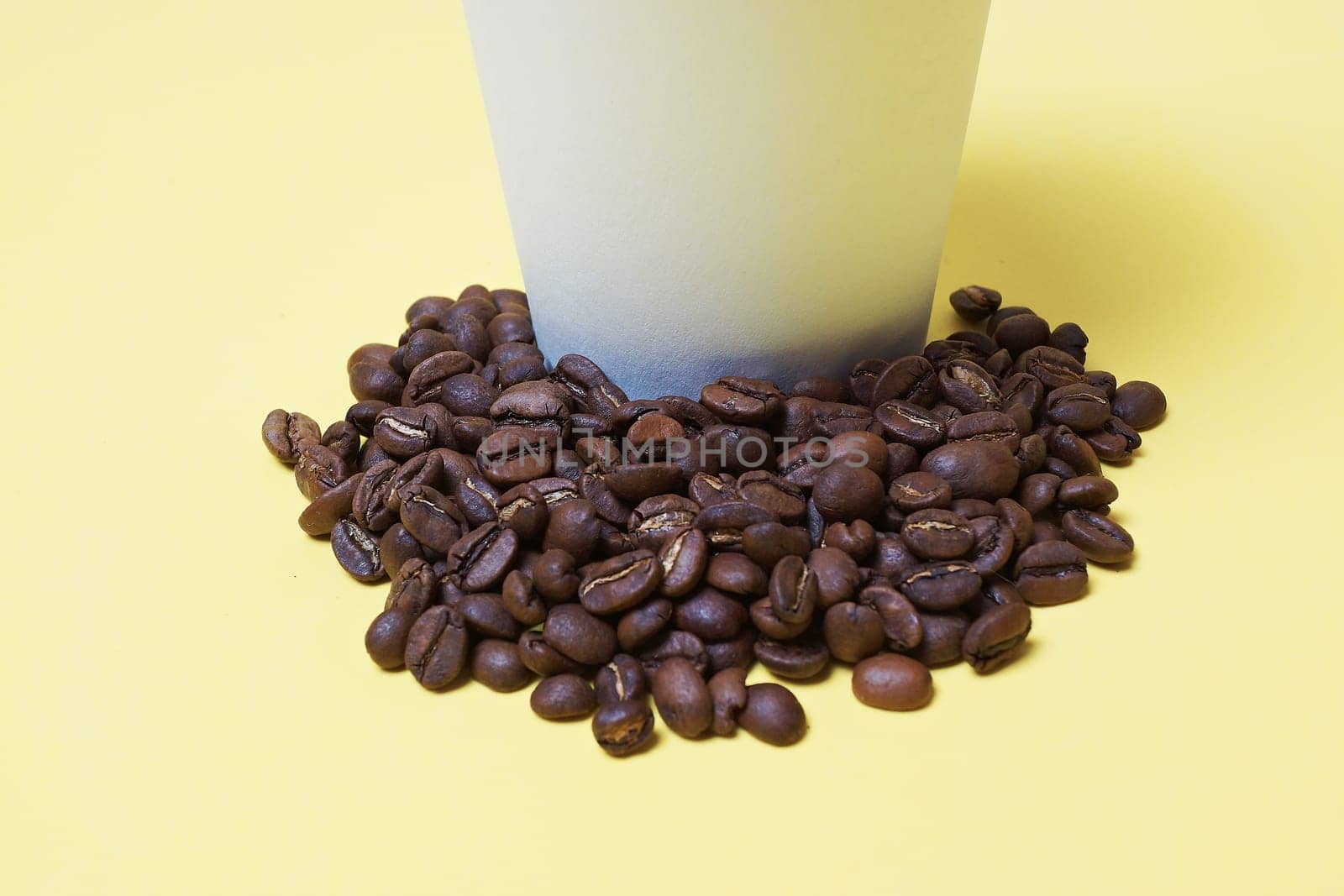 coffee beans next to a paper cup with coffee beans, white,yellow background