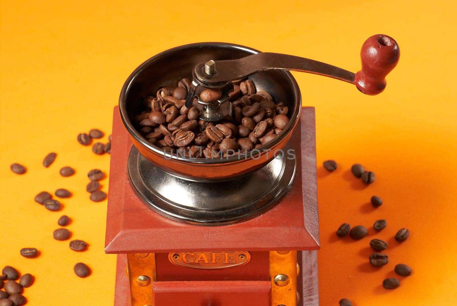 Manual coffee grinder for grinding coffee beans. On an orange background with coffee beans