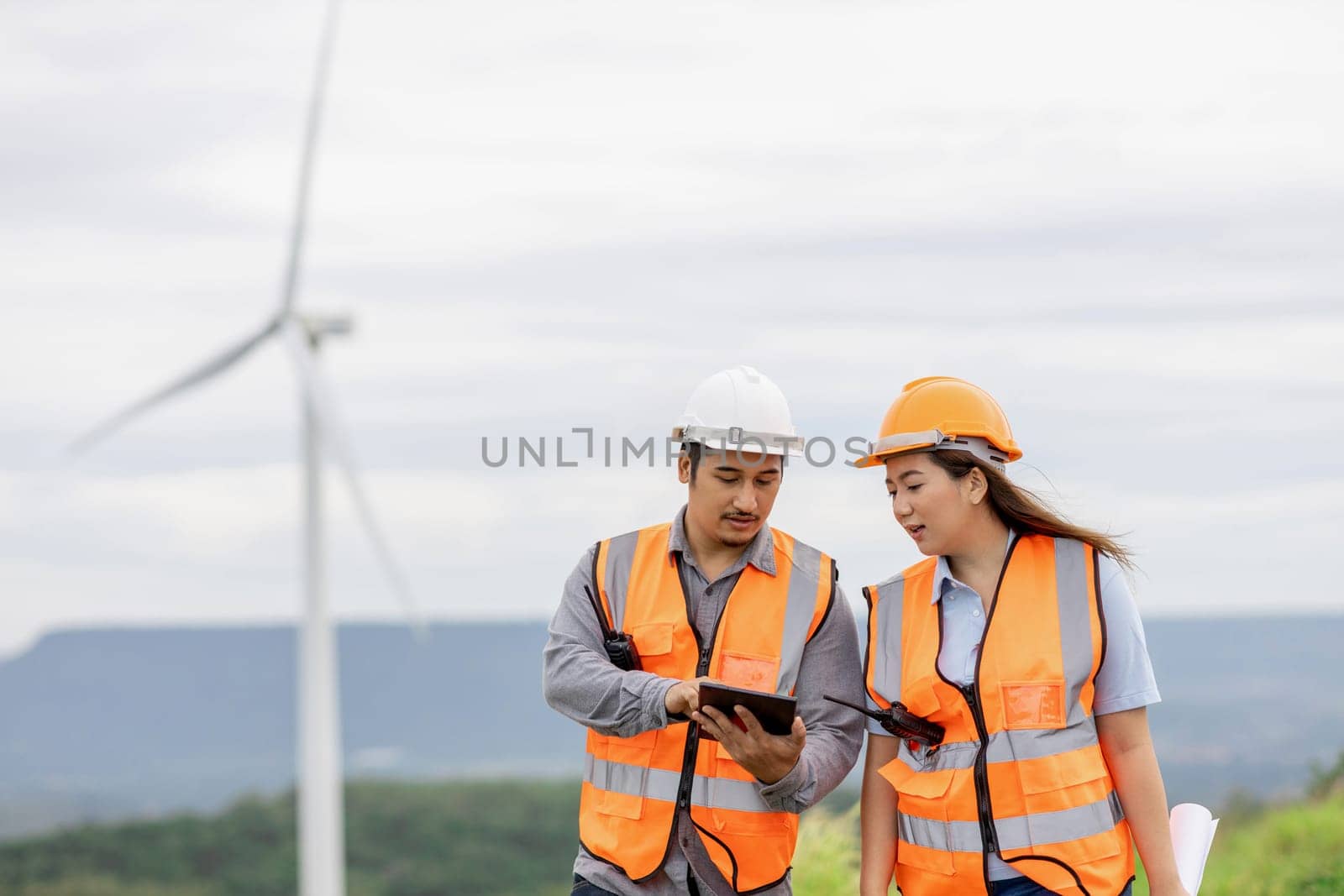 Male and female engineers working on a wind farm atop a hill or mountain in the rural. Progressive ideal for the future production of renewable, sustainable energy.