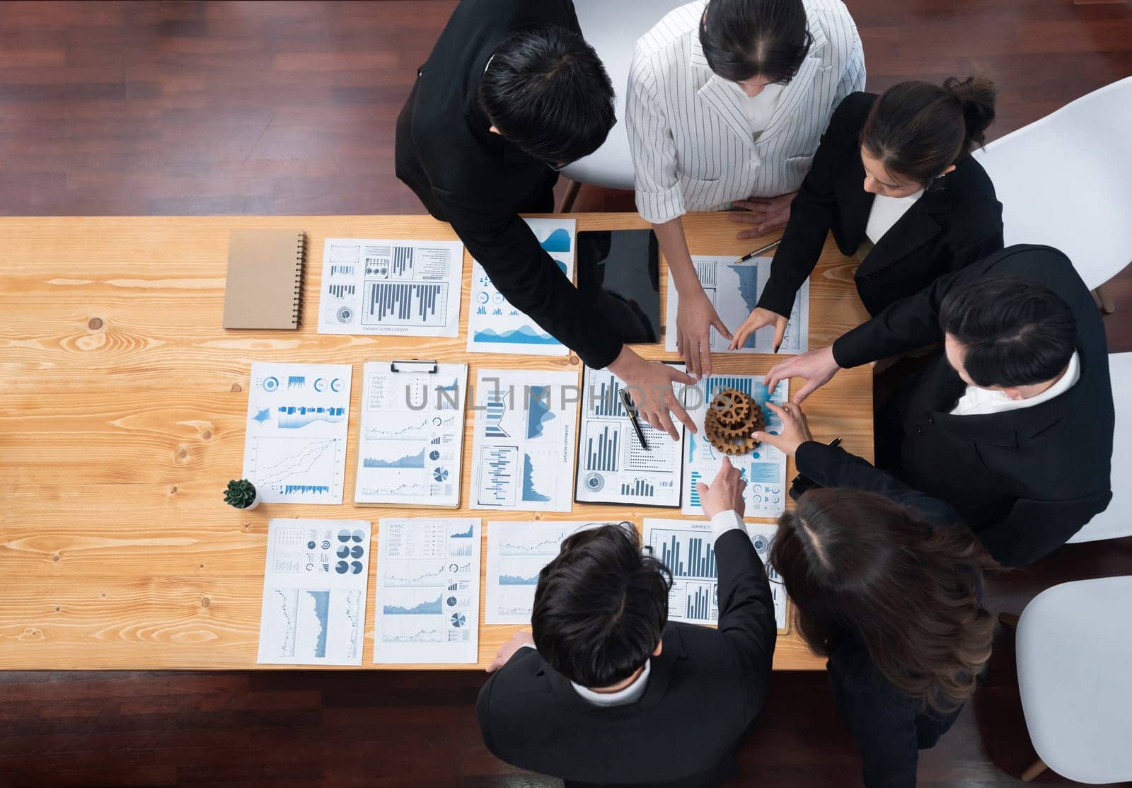 Top view hand holding gear by group of businesspeople on table in harmony office by biancoblue