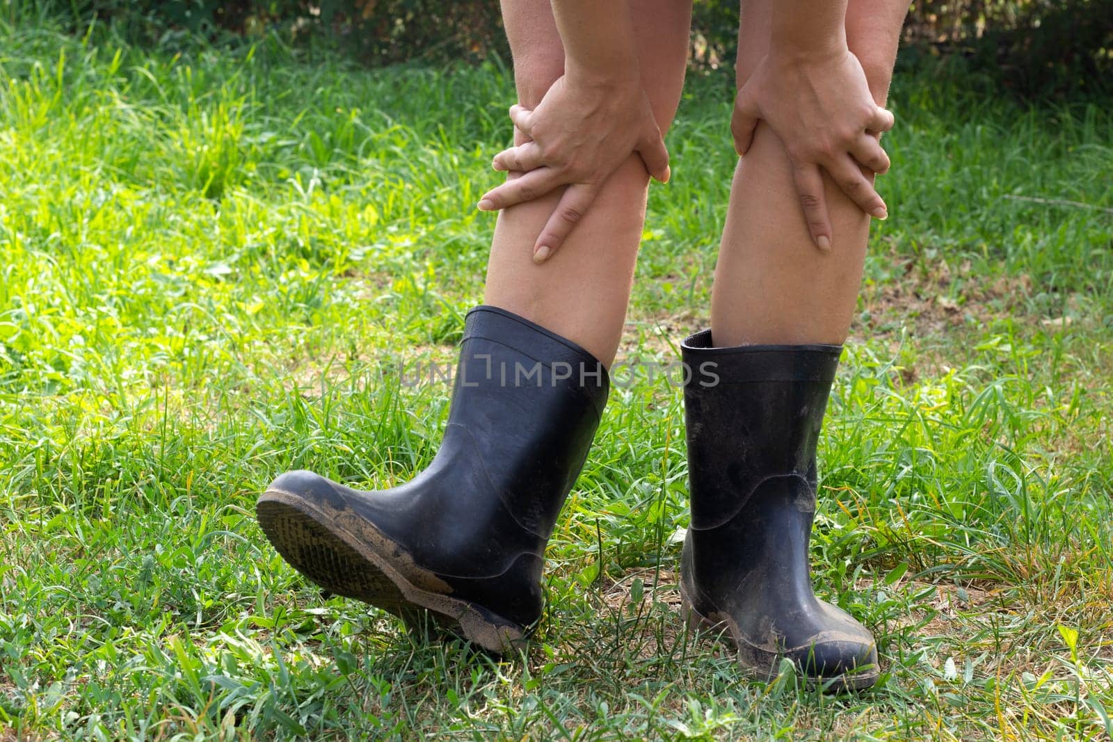 Women's legs in black rubber boots on the background of a green lawn. Summer mood.