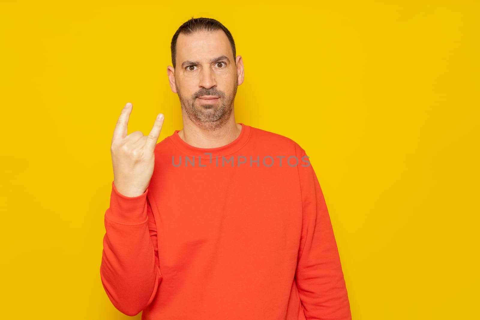 Handsome man wearing sweatshirt over isolated yellow background with crazy expression doing rock symbol with hand up. Music star concept